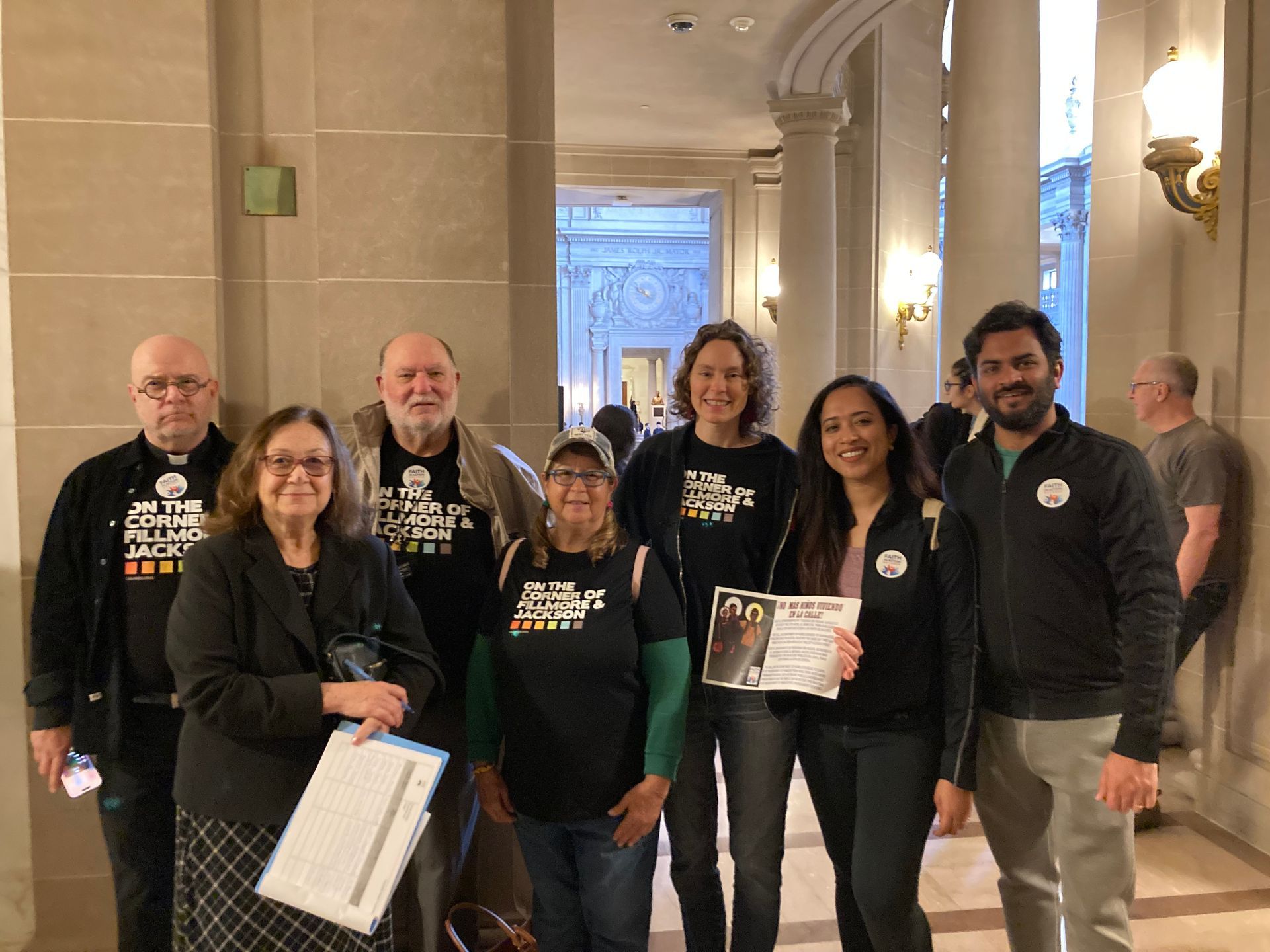 A group of Calvary goers posing for a photo in the hallway of City Hall. Rev. Victor Floyd, Dave, Lupy,  Jane, Alison, Susan, Satyan holding up Faith in Action Bay Area materials about ending child homelessness.