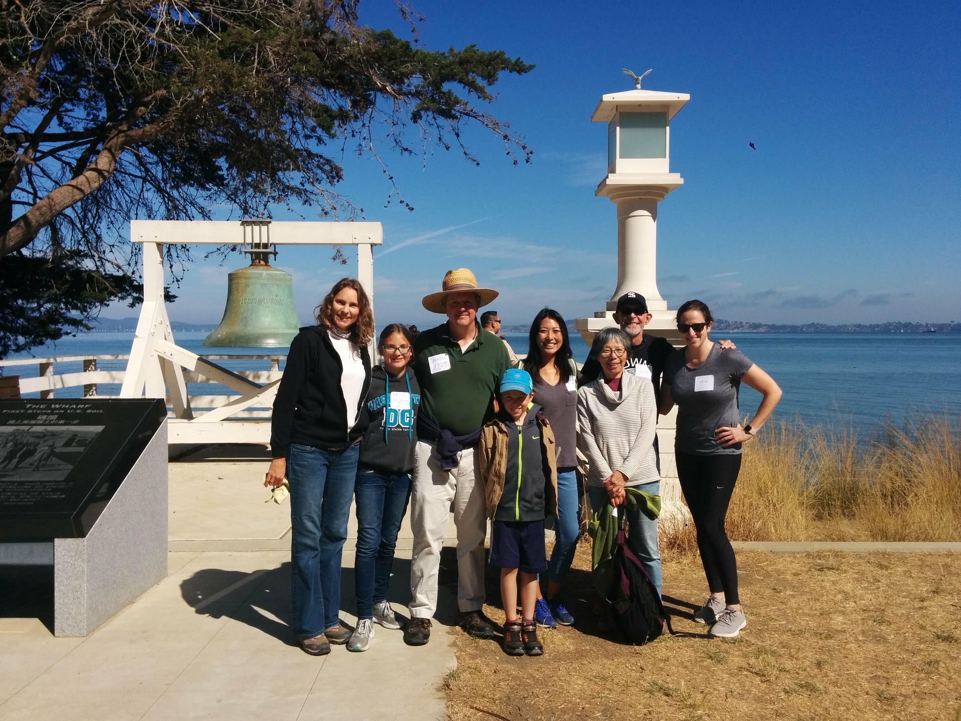 A group of Calvary folks standing in front of a large bell, which is front of a body of water
