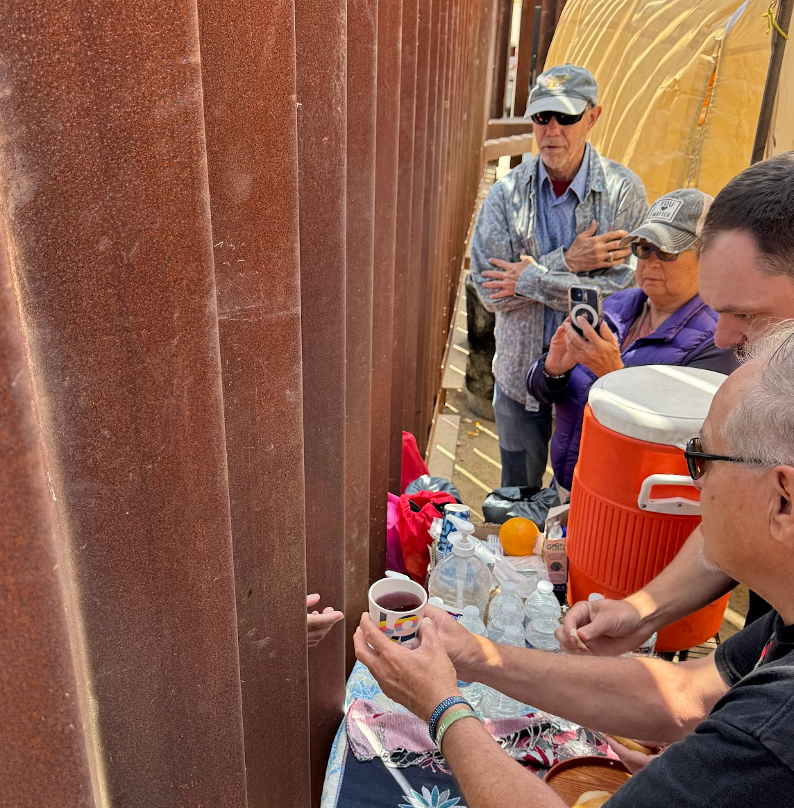 Volunteers at Whiskey 8 Humanitarian Aid site giving communion to a group of migrants on the other side of the wall, awaiting to be taken into processing from border patrol. This is during a worship service. 