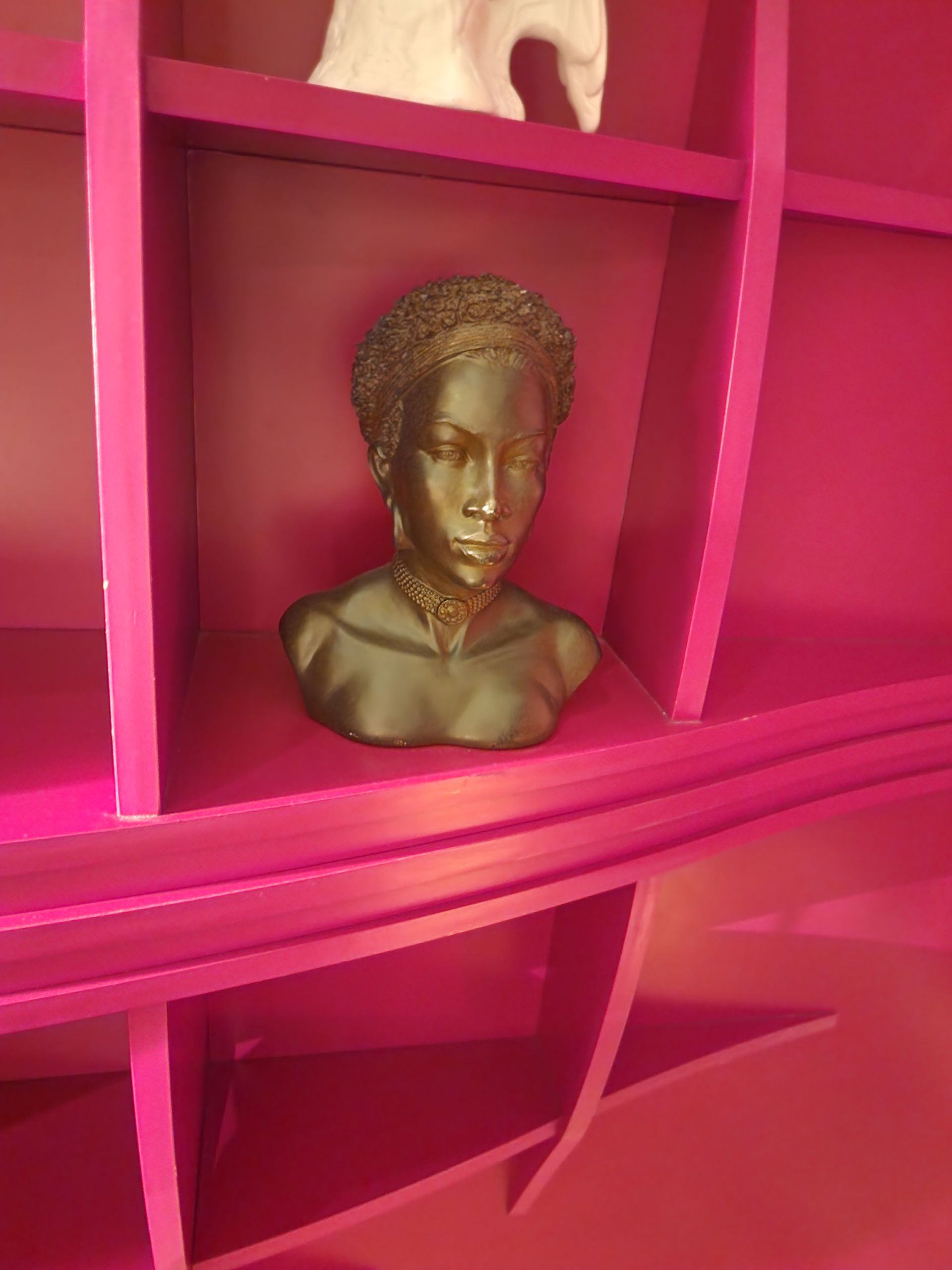 Bronze bust on a pink shelf; the bust has ornate collar and curly hair.