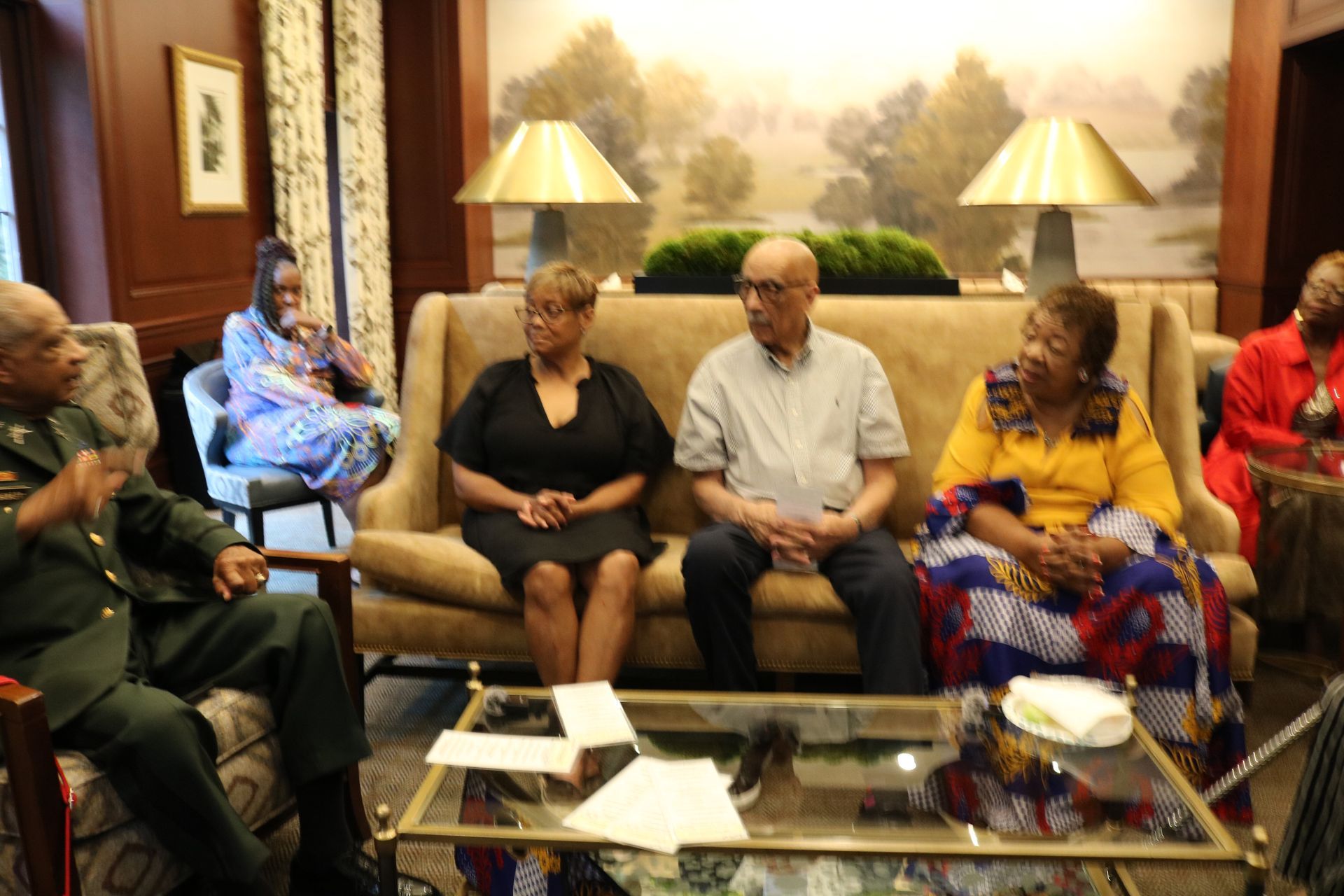 Group of people seated, engaged in conversation in a room with a sofa and artwork on the wall.