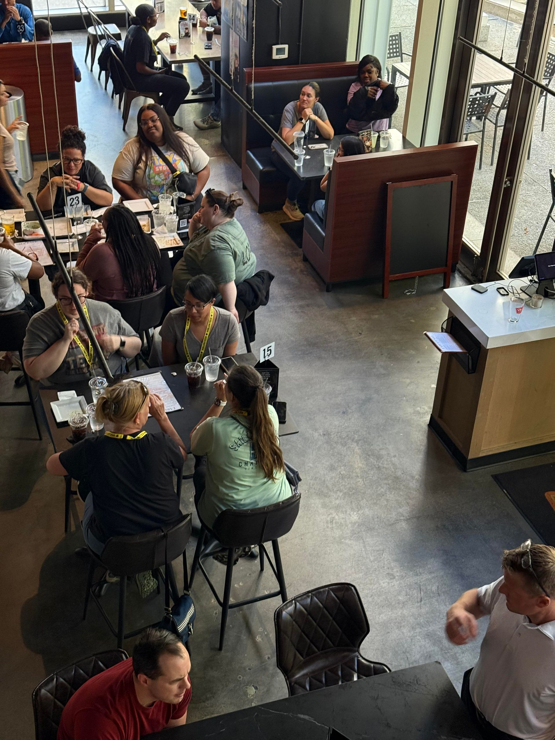 People seated at tables in a brightly lit restaurant, talking and eating, with a server nearby.