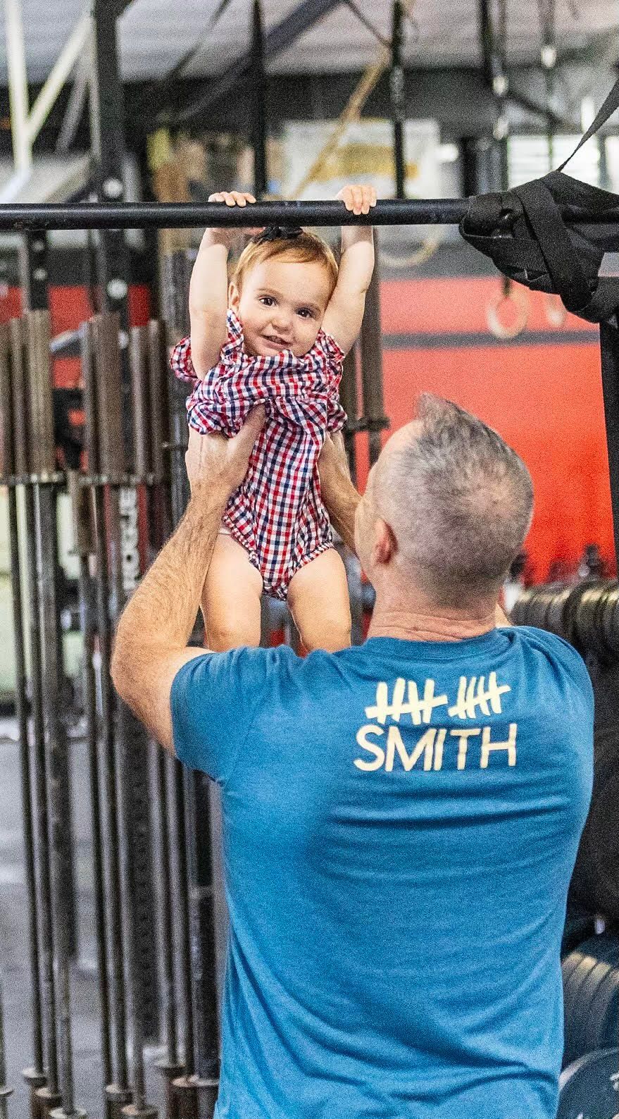 A man is holding a baby on a bar in a gym.