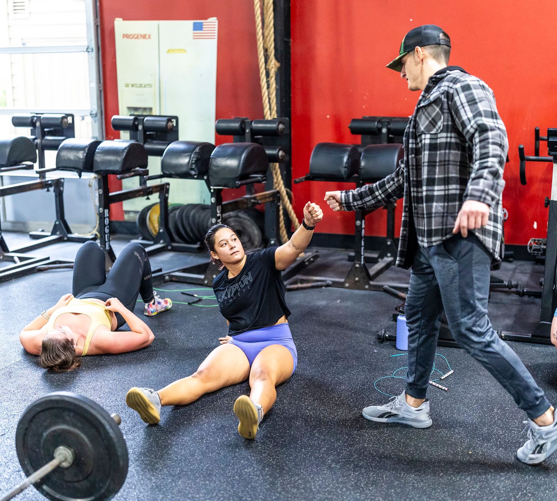A man is talking to a woman who is laying on the floor in a gym.