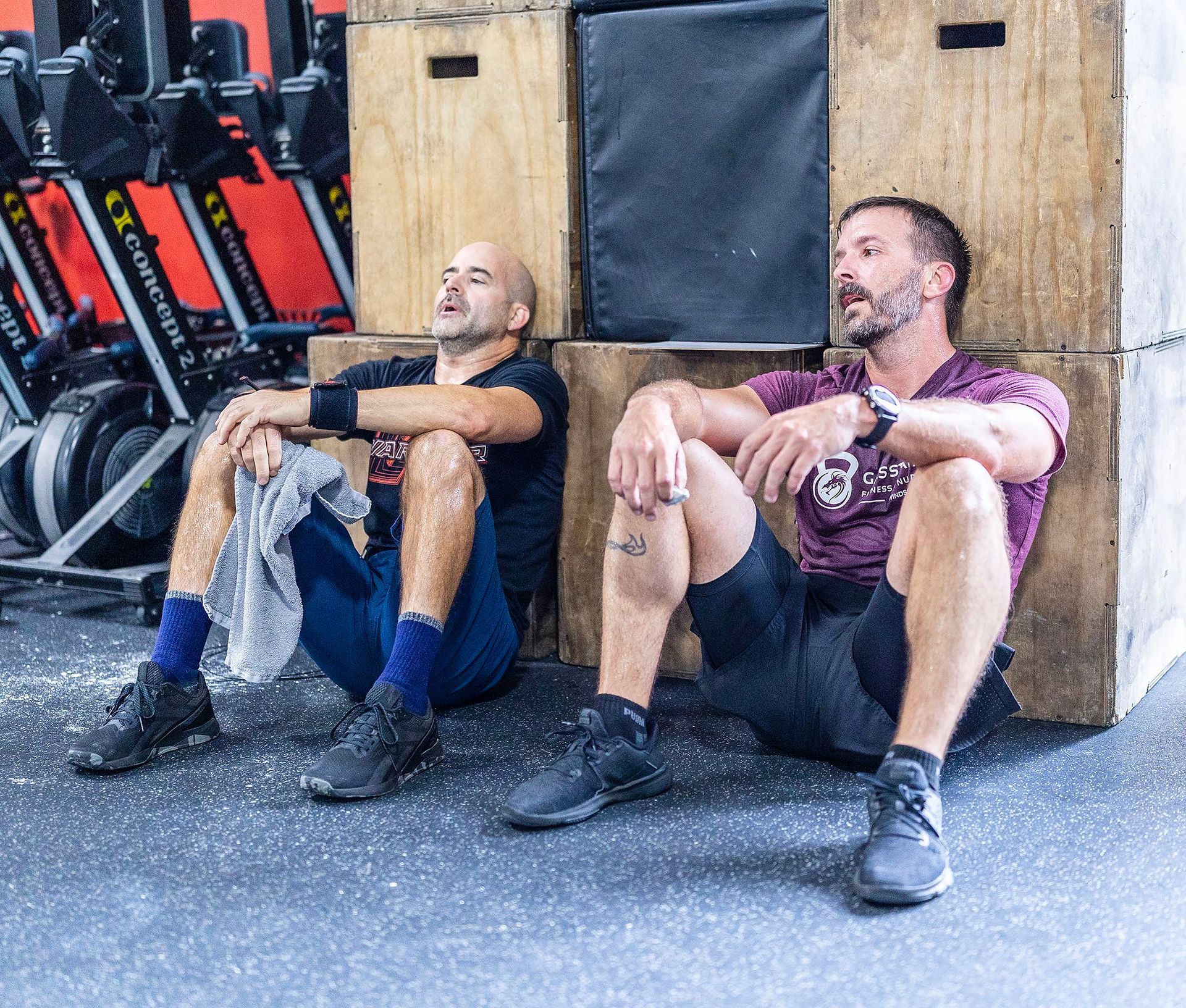 Two men are sitting on a box in a gym.