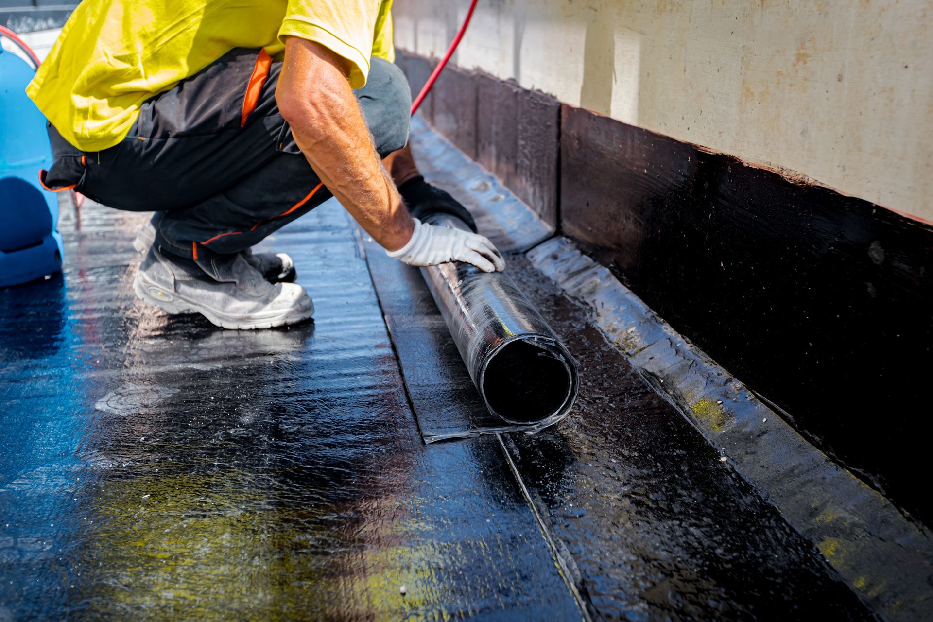 Worker applying black waterproof coating to a flat roof with a roller brush
