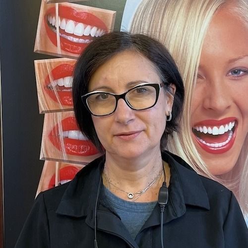 Woman with glasses standing before a dental poster showing smiling teeth and a blonde model