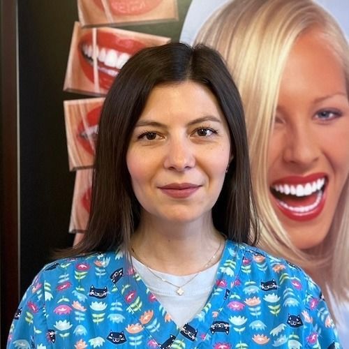 Woman in blue patterned scrubs standing before a dental smile poster backdrop