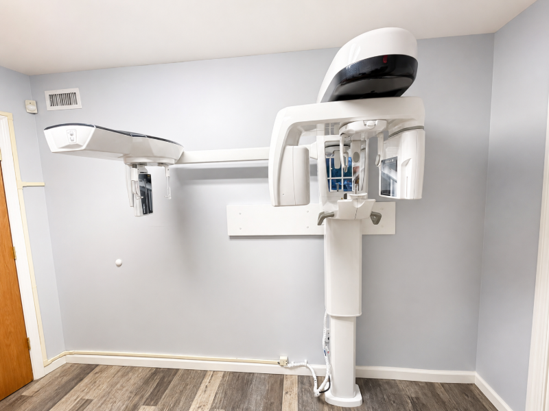 Dental X-ray machine in a clinic room with light gray walls and wood flooring