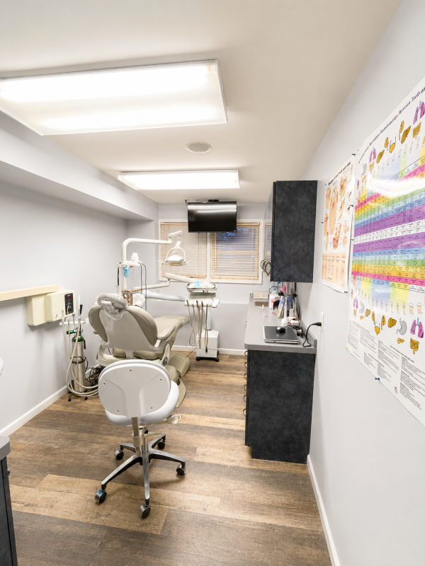 Modern dental exam room with chair, overhead light, sink, and wall-mounted monitor