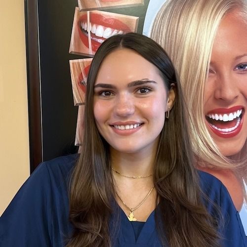 Woman smiling in a navy top, standing indoors in front of a dental poster.