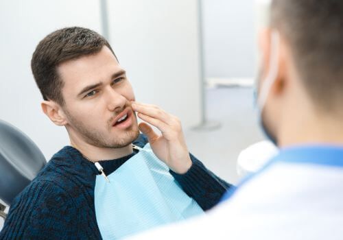 Man at dentist with blue bib holding cheek while speaking to clinician