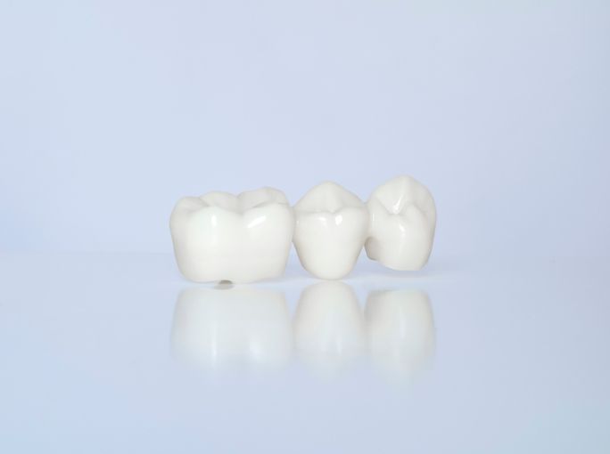 Three white ceramic dental crowns on a pale blue background