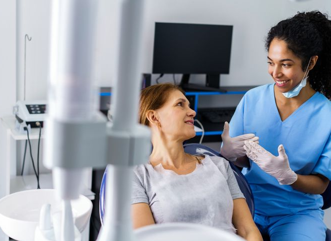 Dentist in blue scrubs talking to a reclining patient in a dental clinic