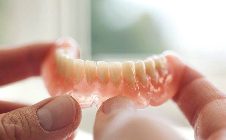 Hands holding a clear dental aligner with aligned teeth impressions against a blurred background