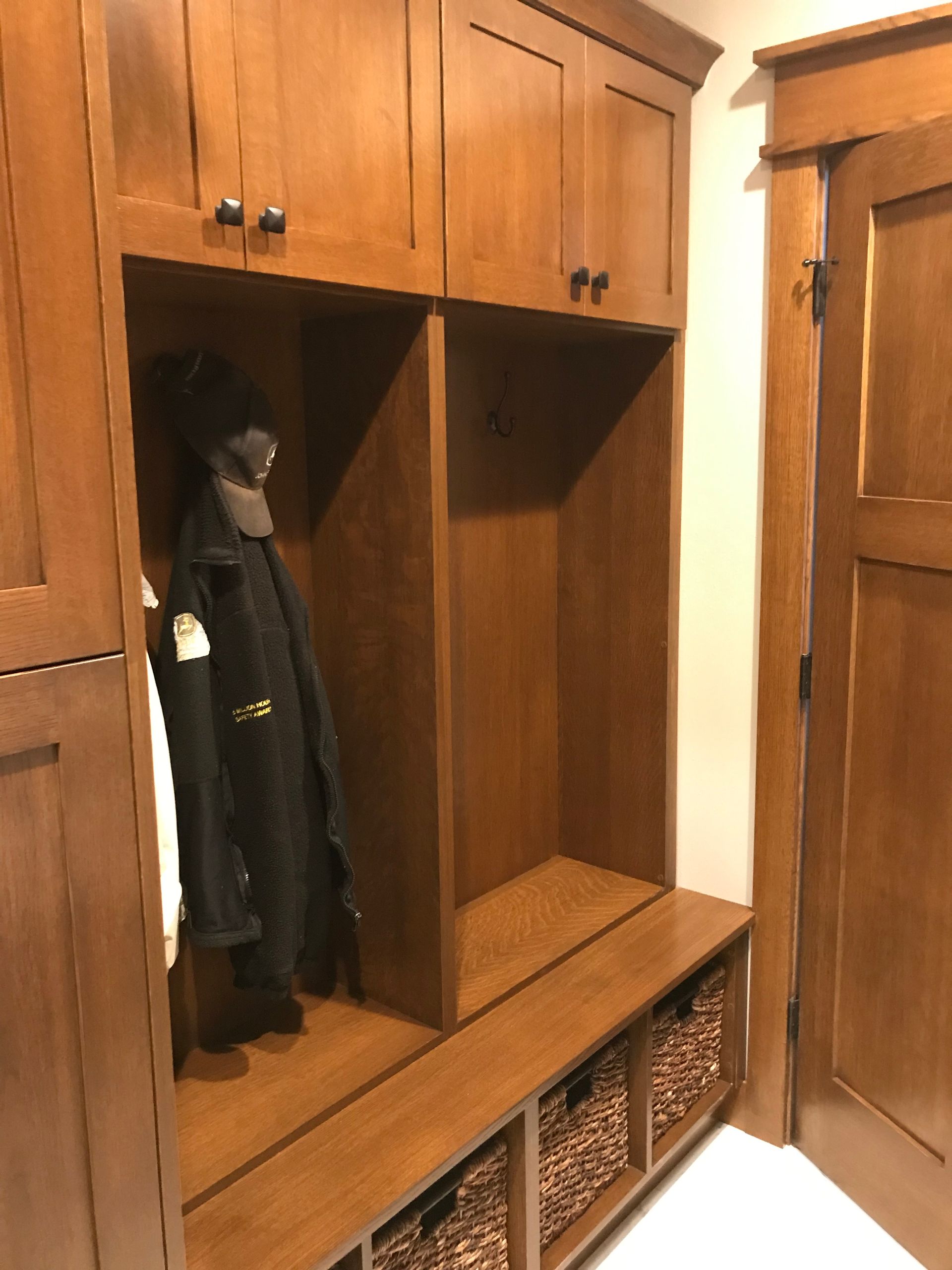 A coat is hanging in a wooden locker in a hallway.