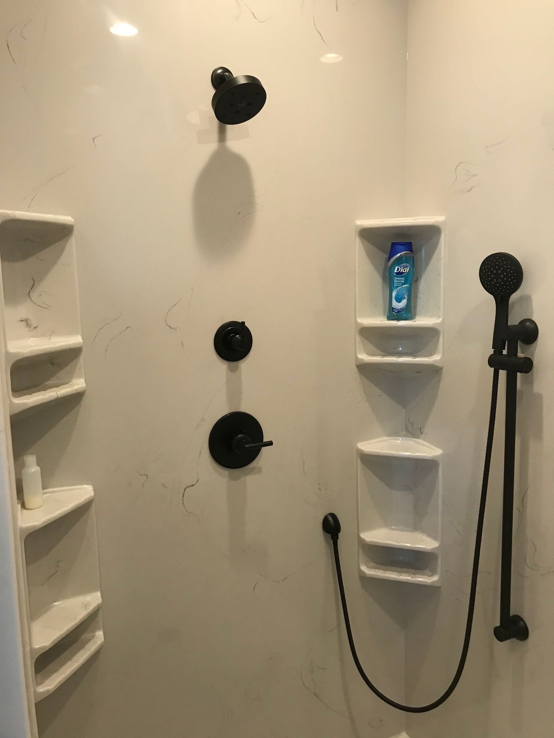 A shower with a black shower head and shelves.