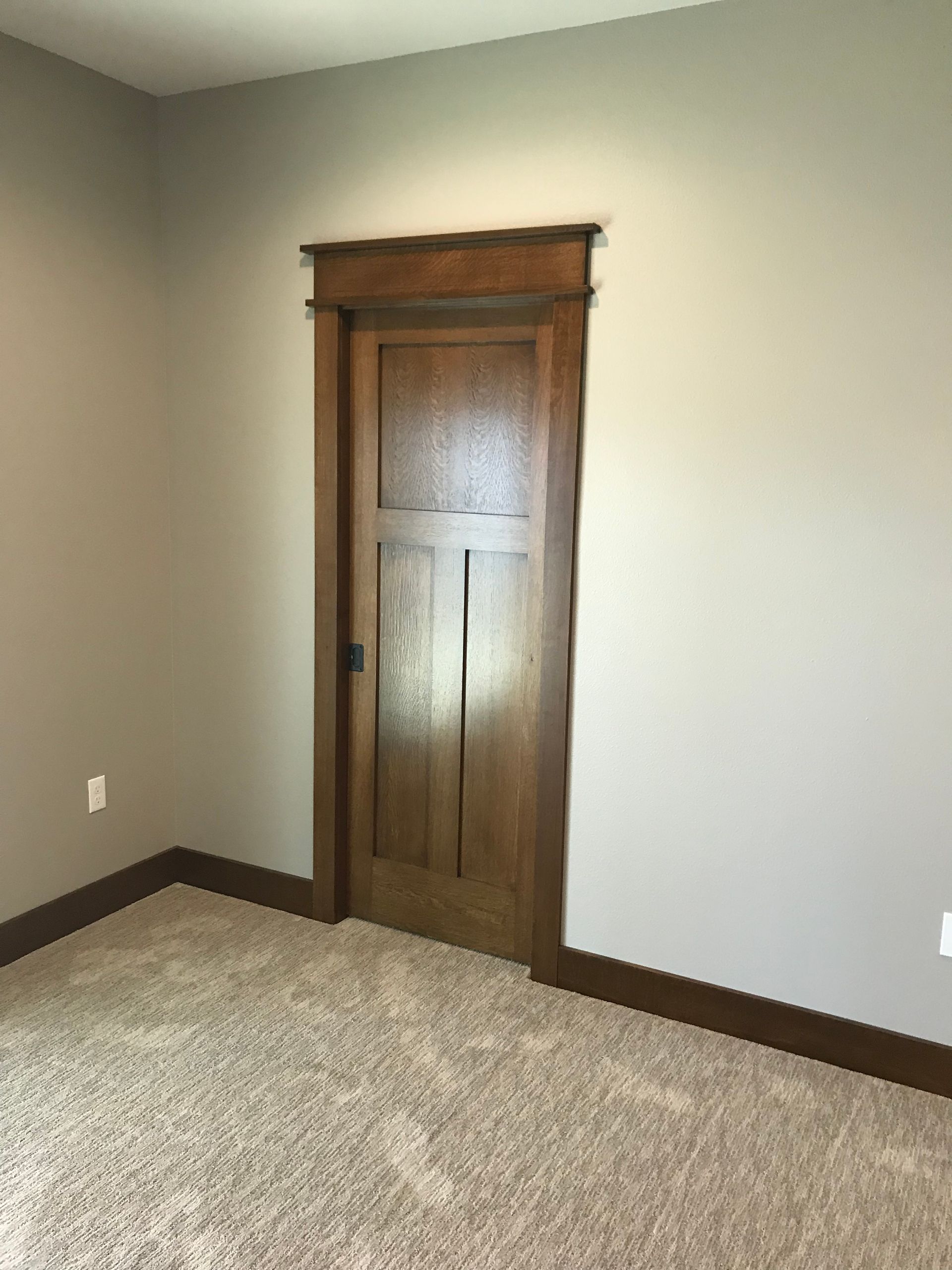 An empty room with a wooden door and a carpeted floor.