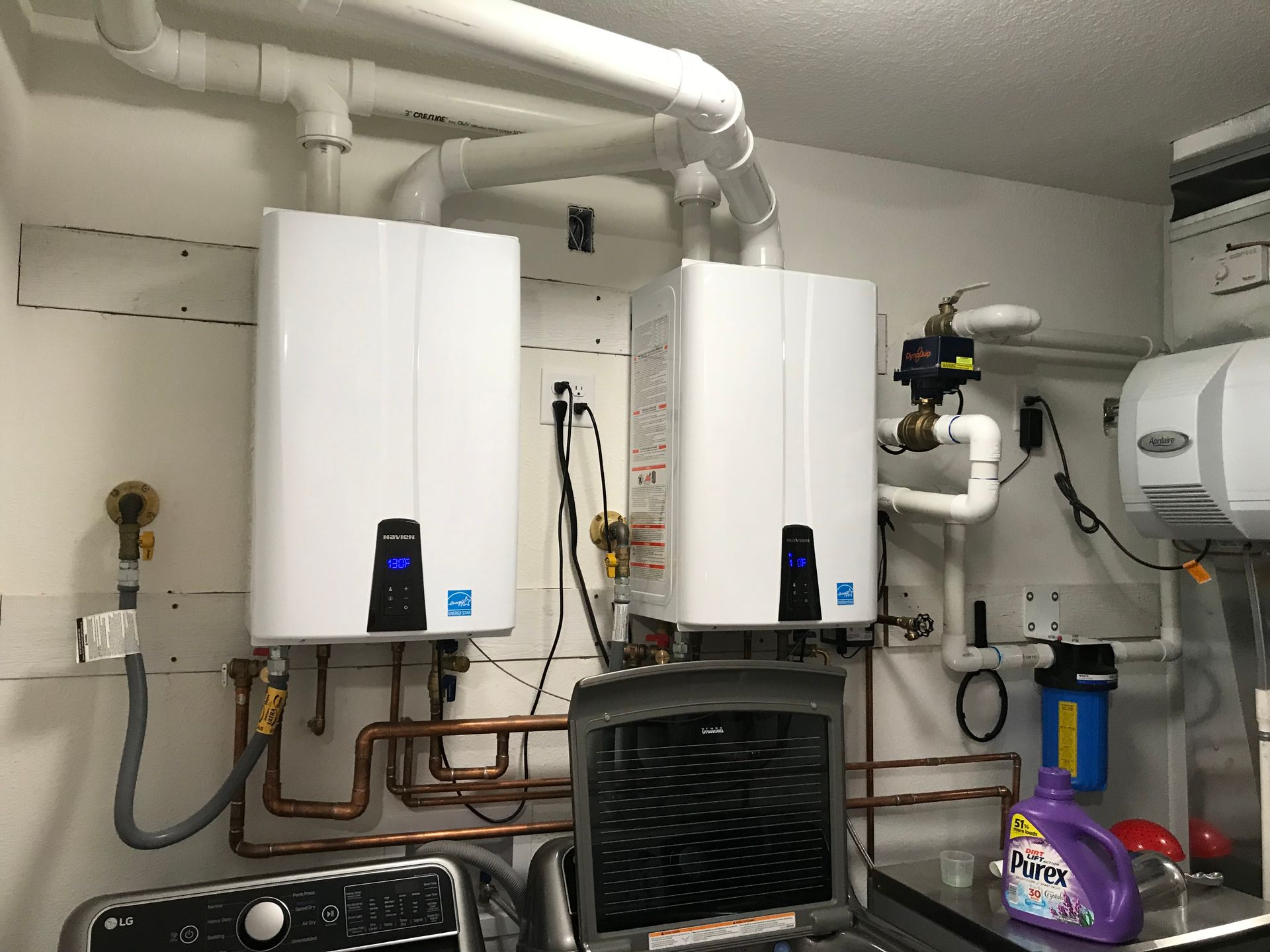 Two water heaters are hanging on the wall in a laundry room.