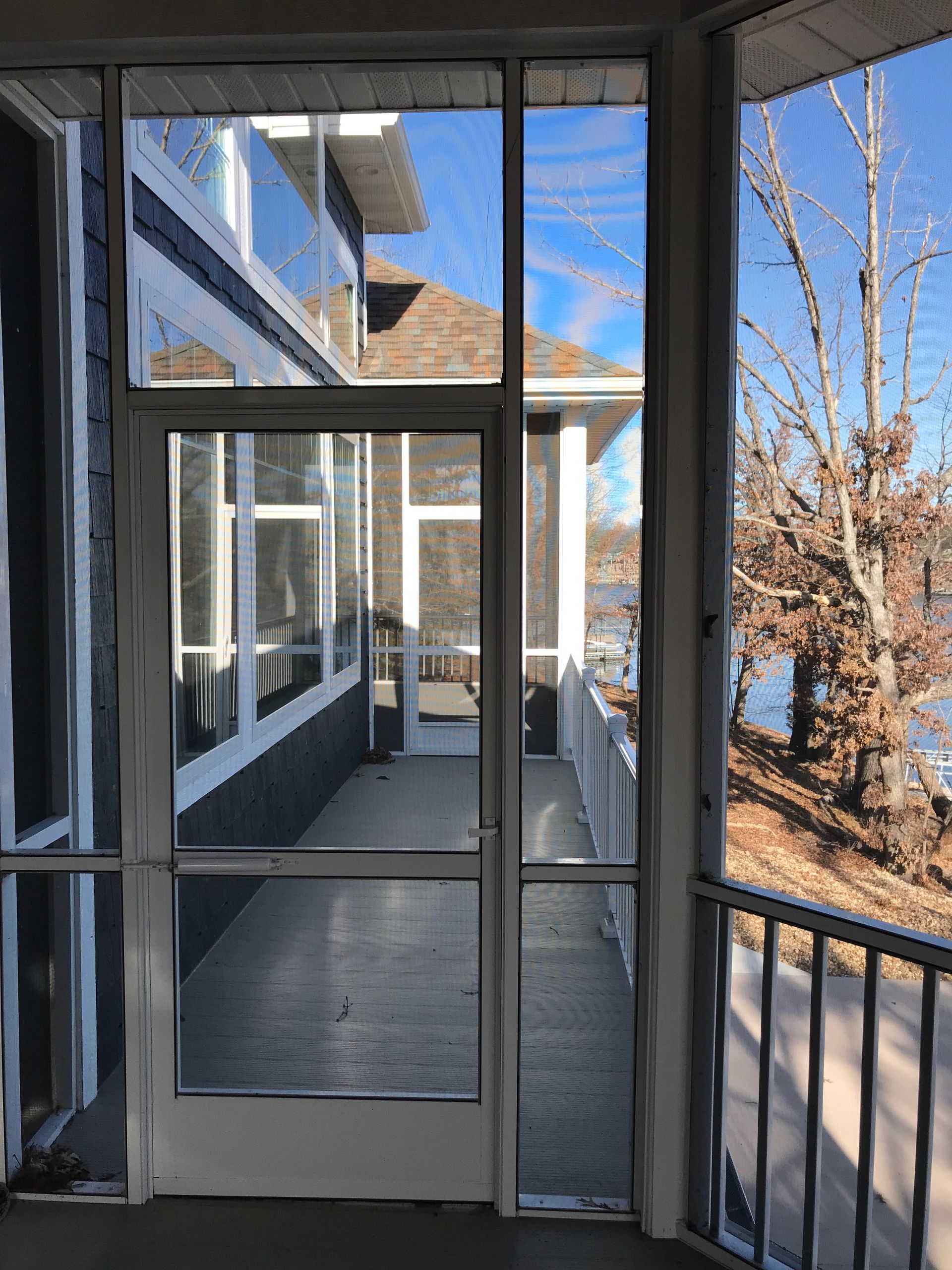 A screened in porch with a view of a house and a lake.