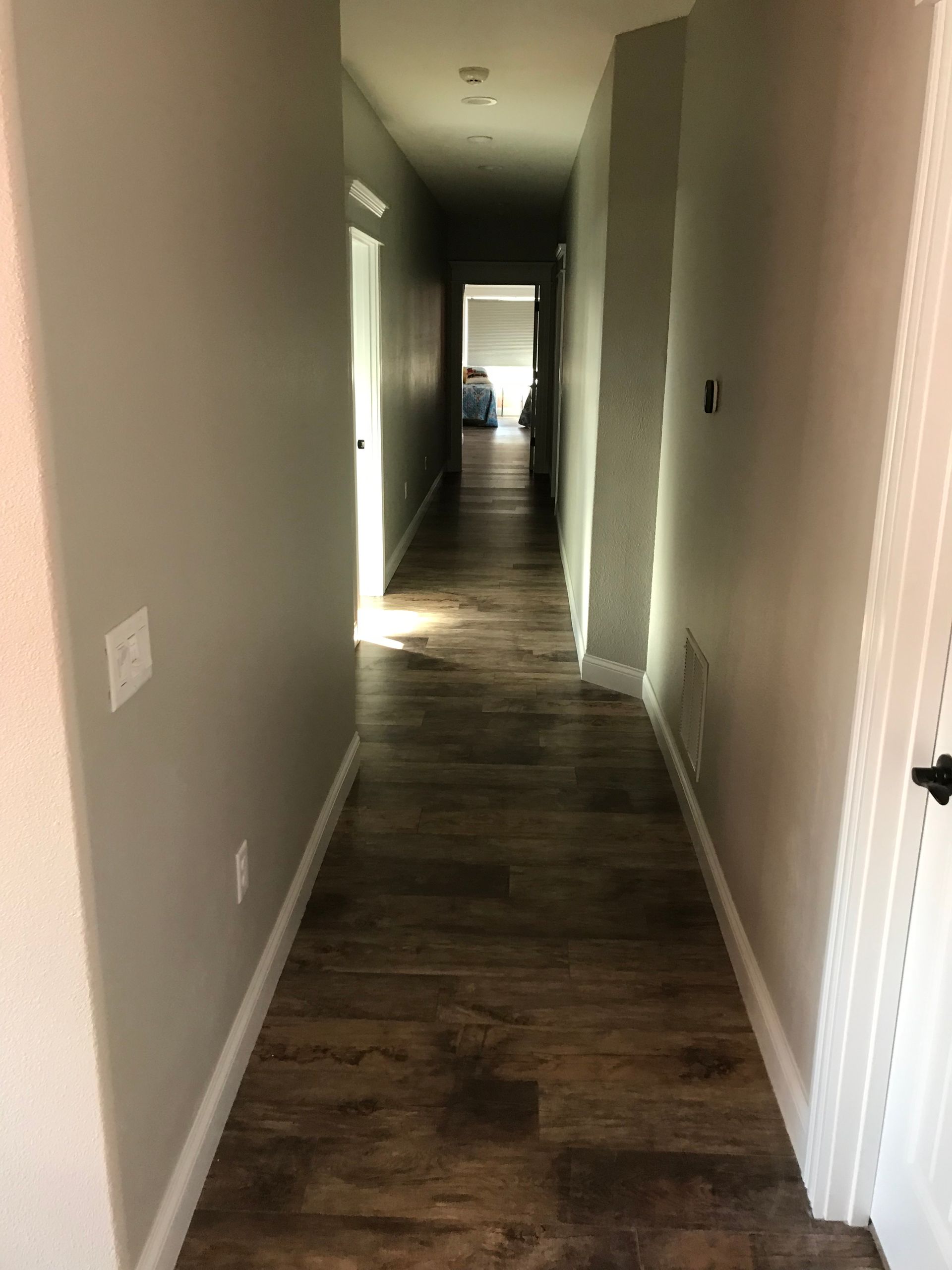 A long hallway with hardwood floors and gray walls in a house.