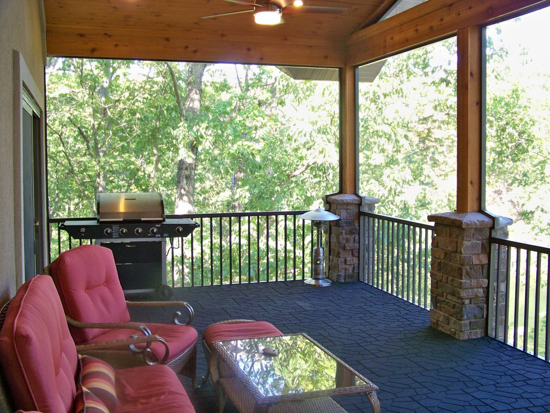 A screened in porch with red chairs and a grill