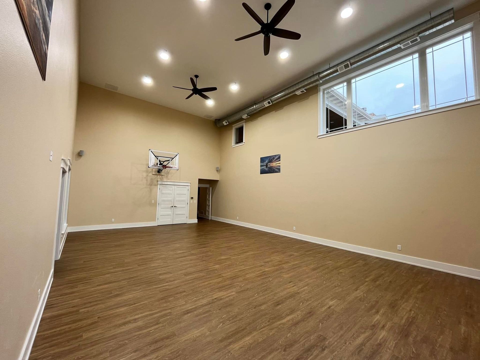 A large empty room with a wooden floor and ceiling fans.