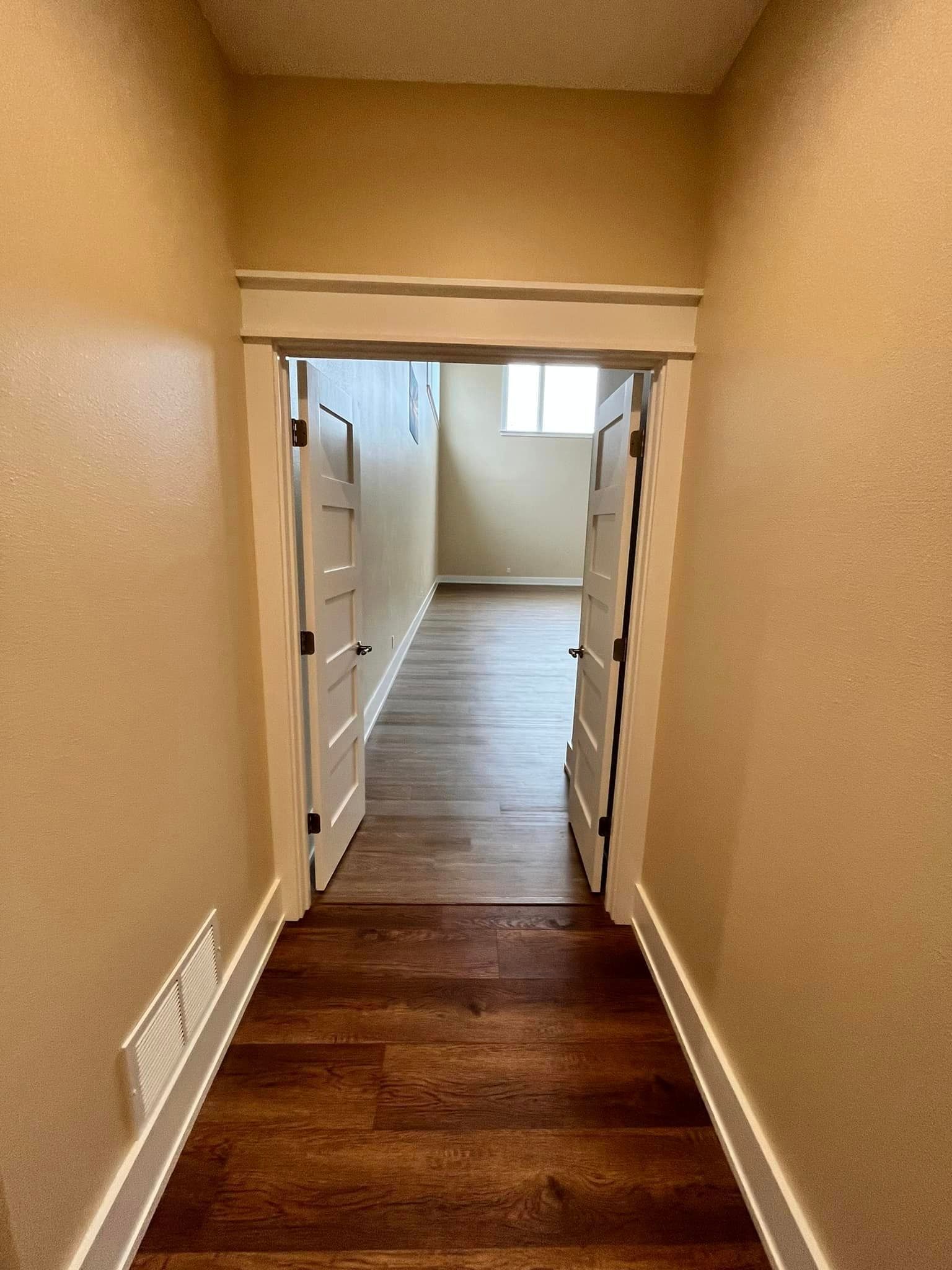 A hallway with hardwood floors and a door that is open leading to a room.
