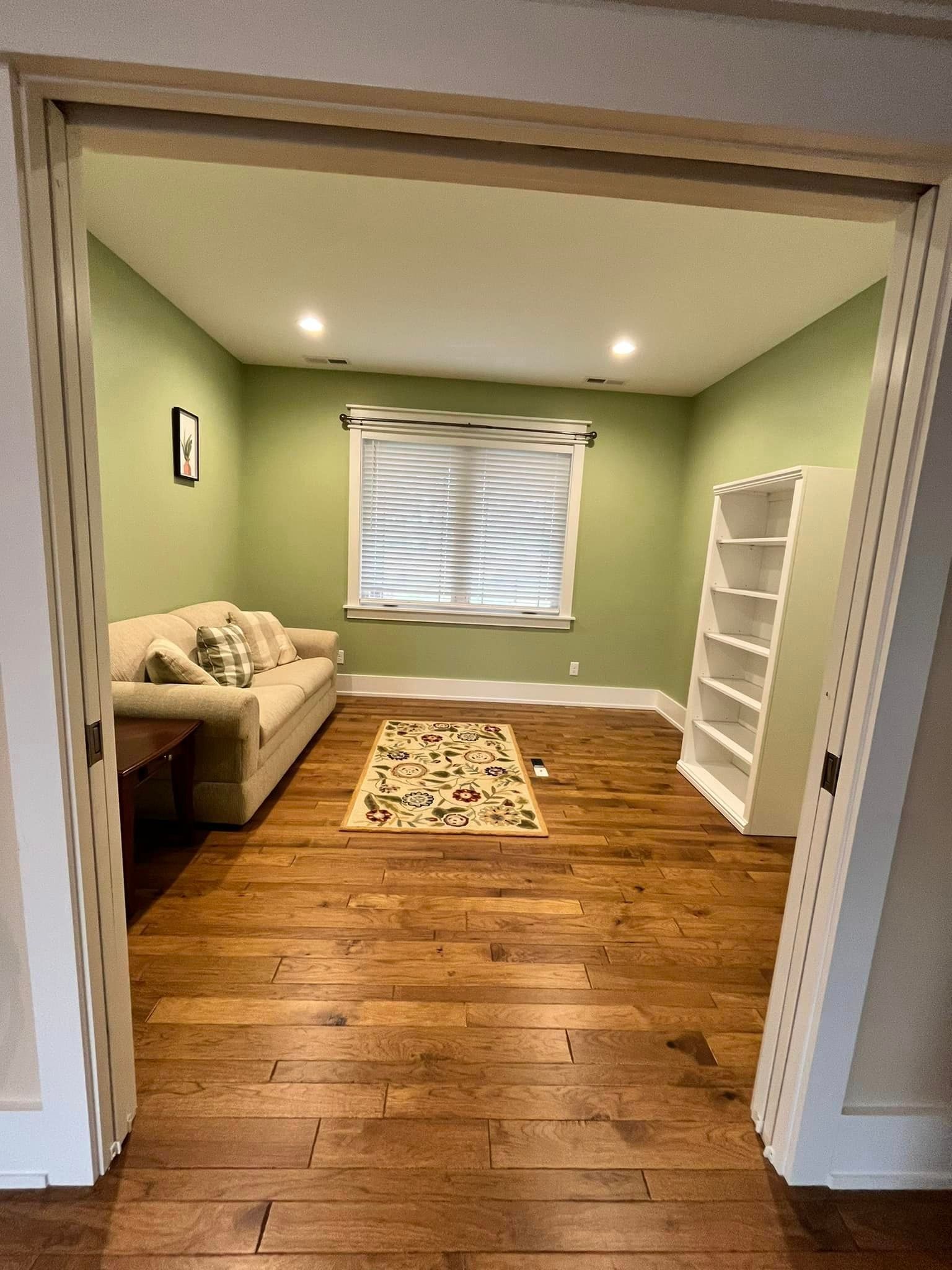 A living room with green walls , hardwood floors , a couch and a bookshelf.