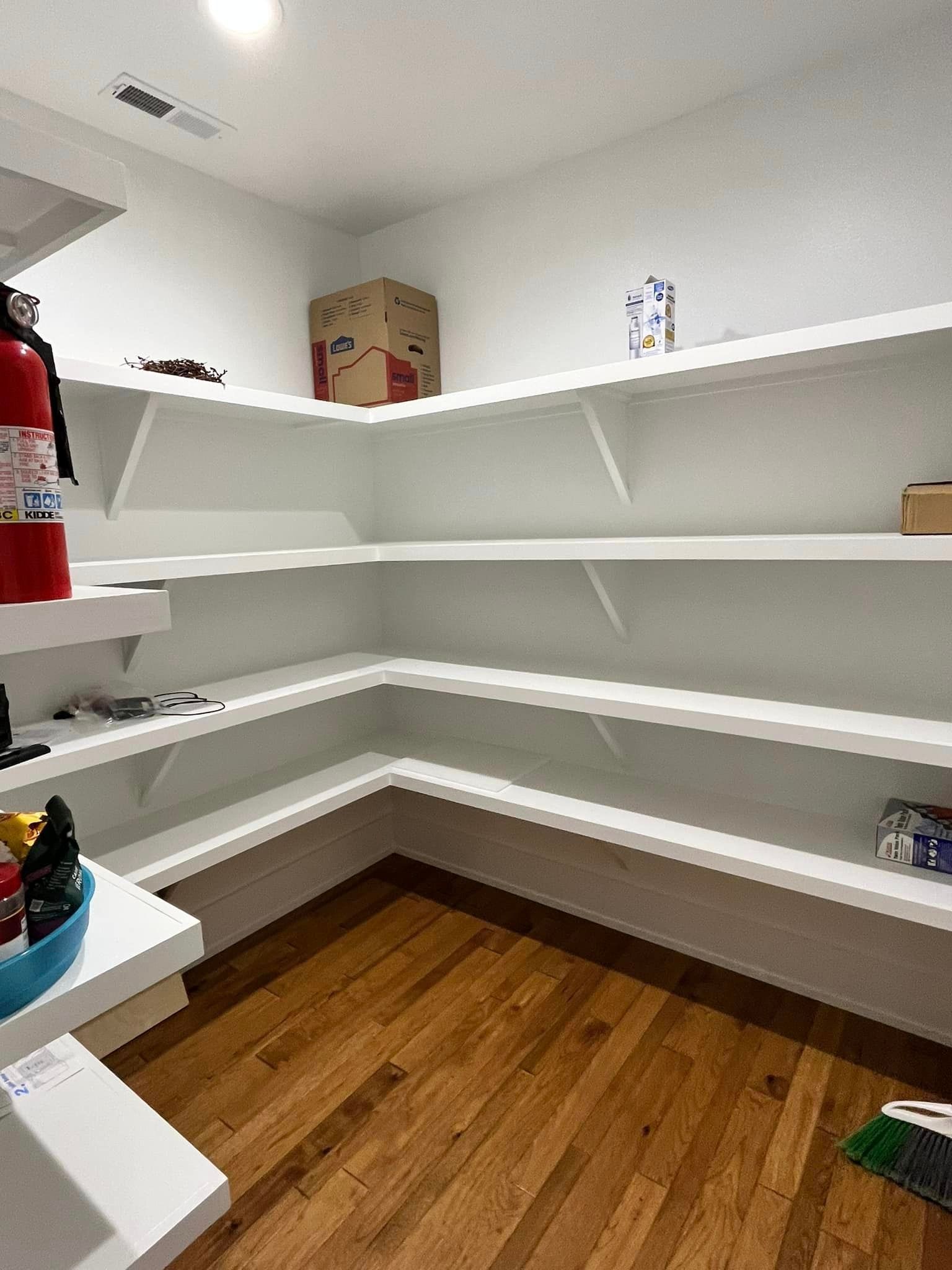 An empty pantry with wooden floors and white shelves.