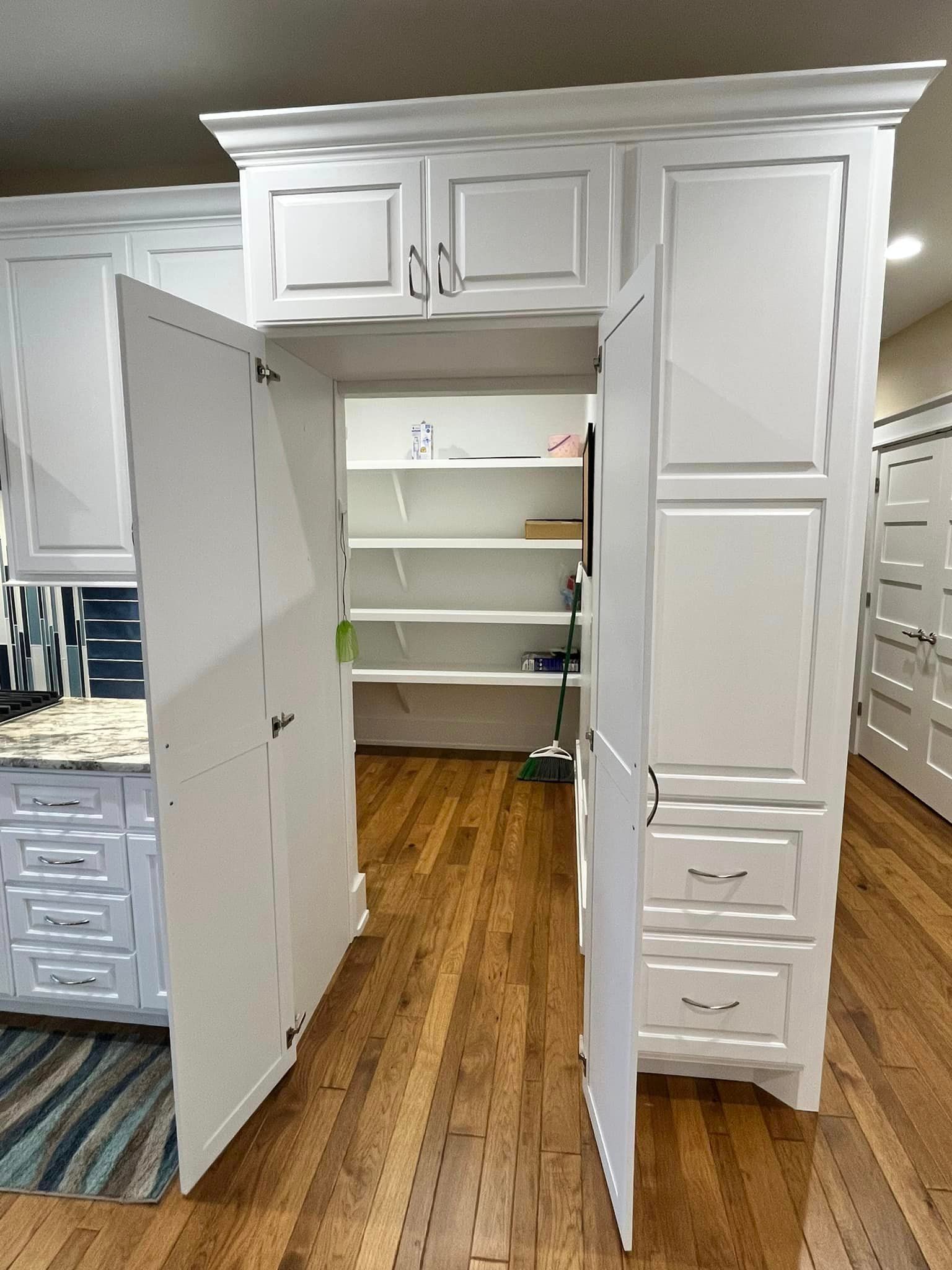 A kitchen with white cabinets and wooden floors with the doors open.
