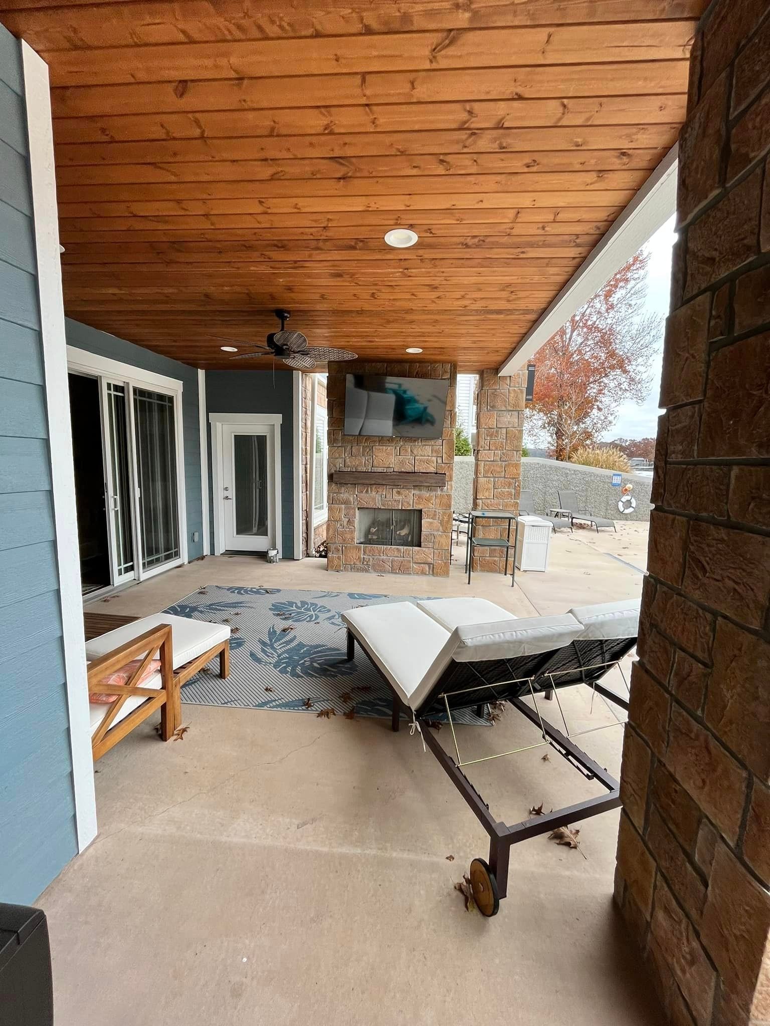 A patio with a fireplace and chairs under a wooden ceiling.