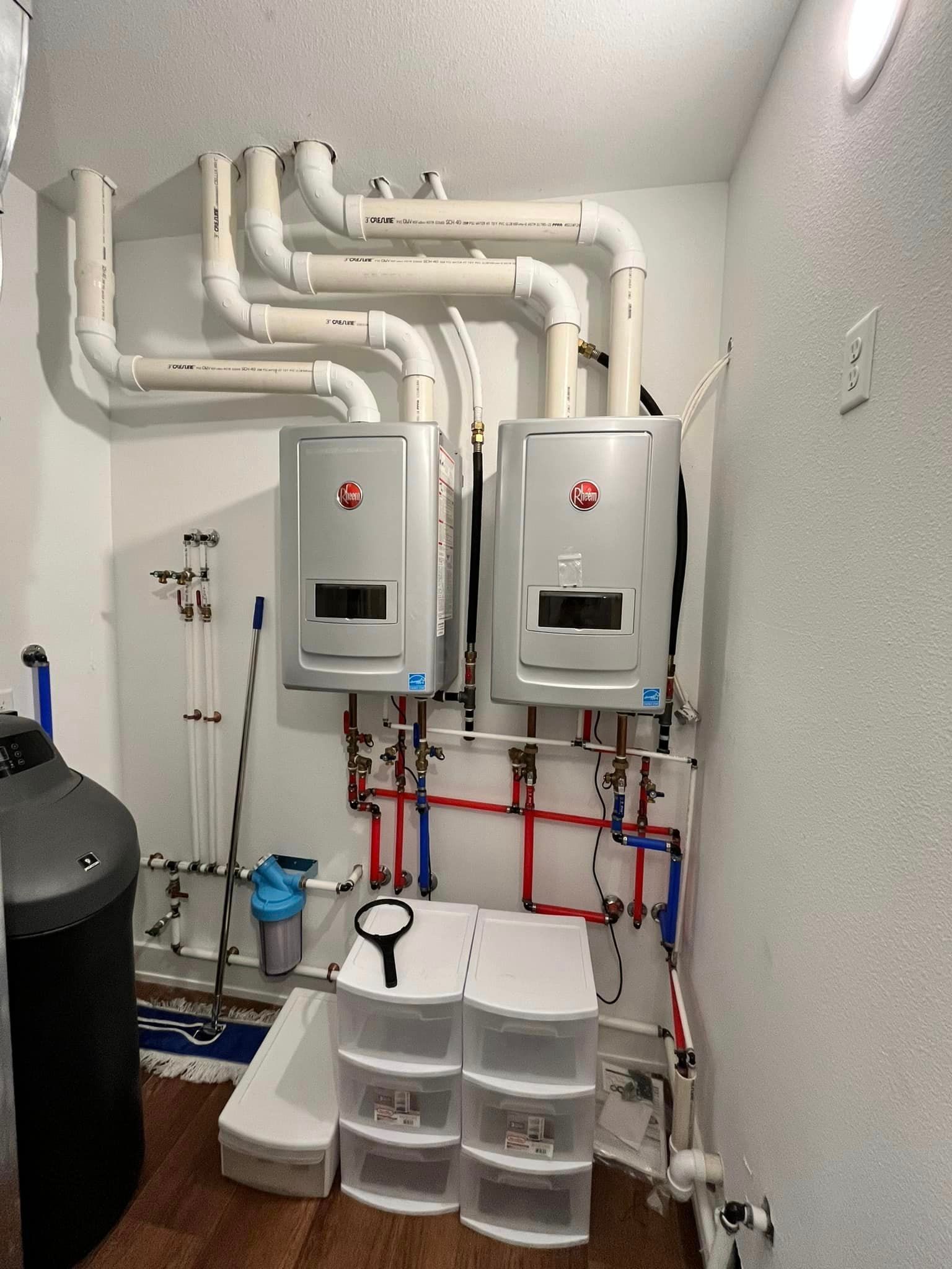 A room with two water heaters and pipes hanging from the ceiling.