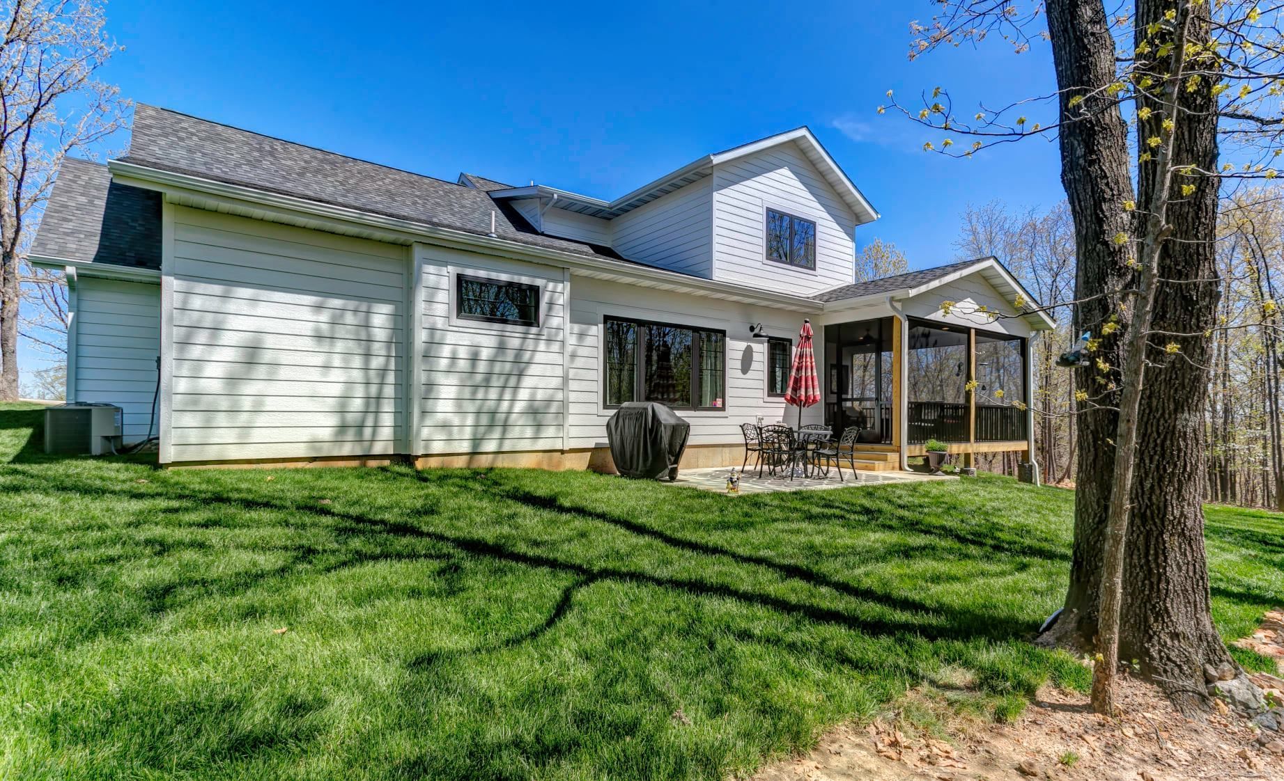 The back of a house with a screened in porch and a large lawn.