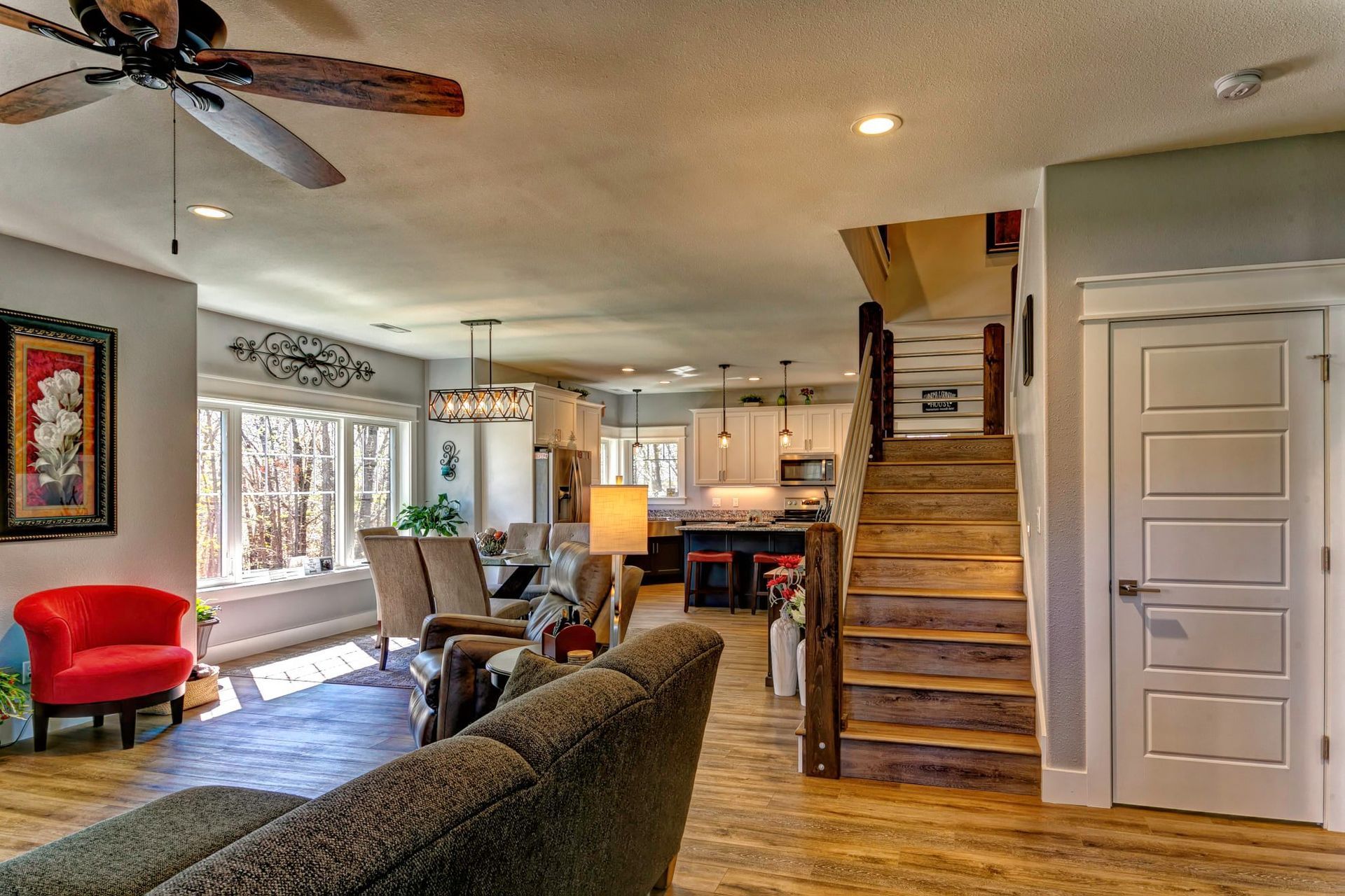 A living room with a couch , chairs , stairs and a ceiling fan.