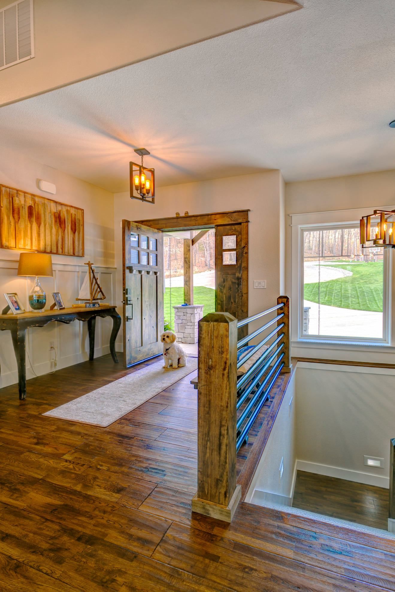 A dog is sitting in a hallway next to a staircase in a house.