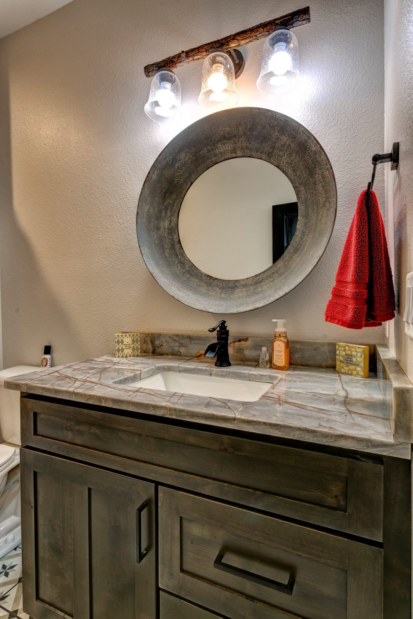 A bathroom with a sink , mirror and towel hanging on the wall.