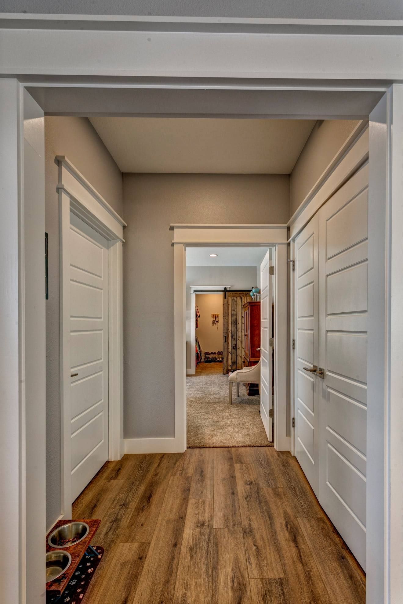 A hallway with hardwood floors and white doors leading to a bedroom.