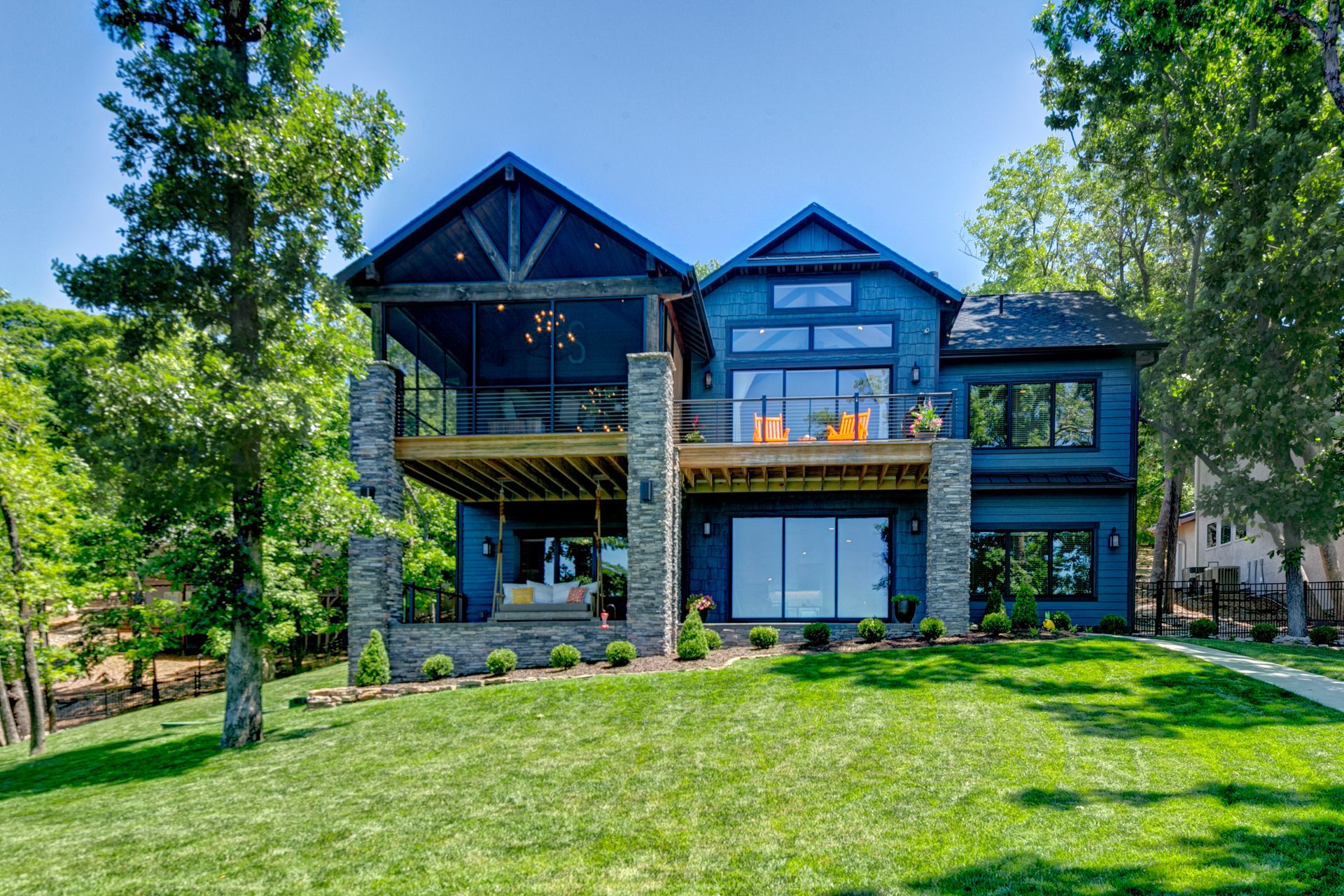 A large blue house is sitting on top of a lush green hill surrounded by trees.