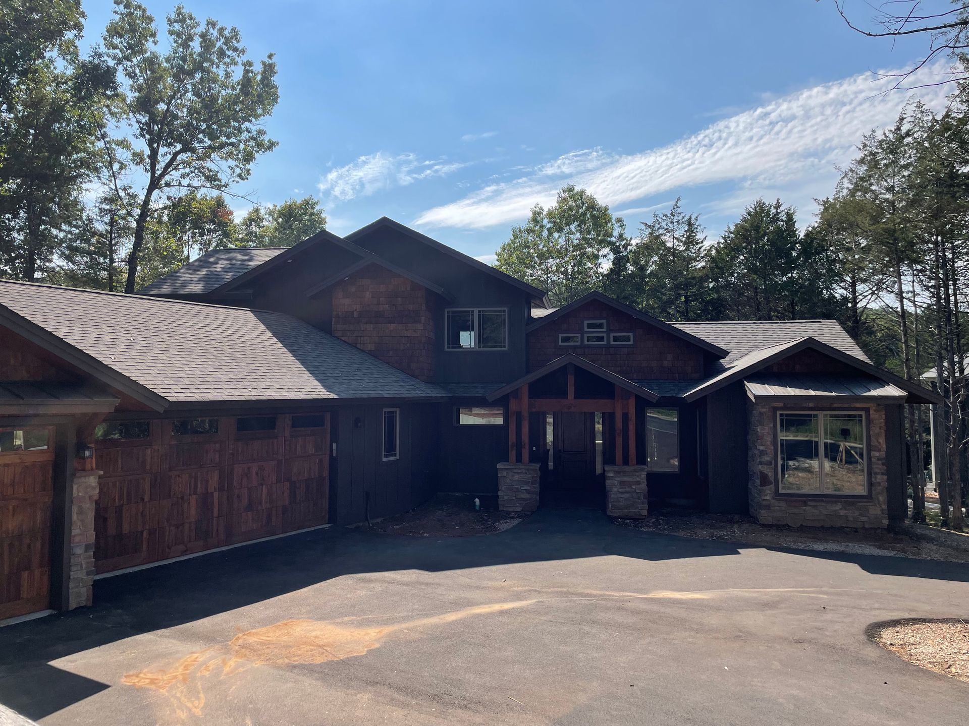 A large house with a garage and a driveway is surrounded by trees.