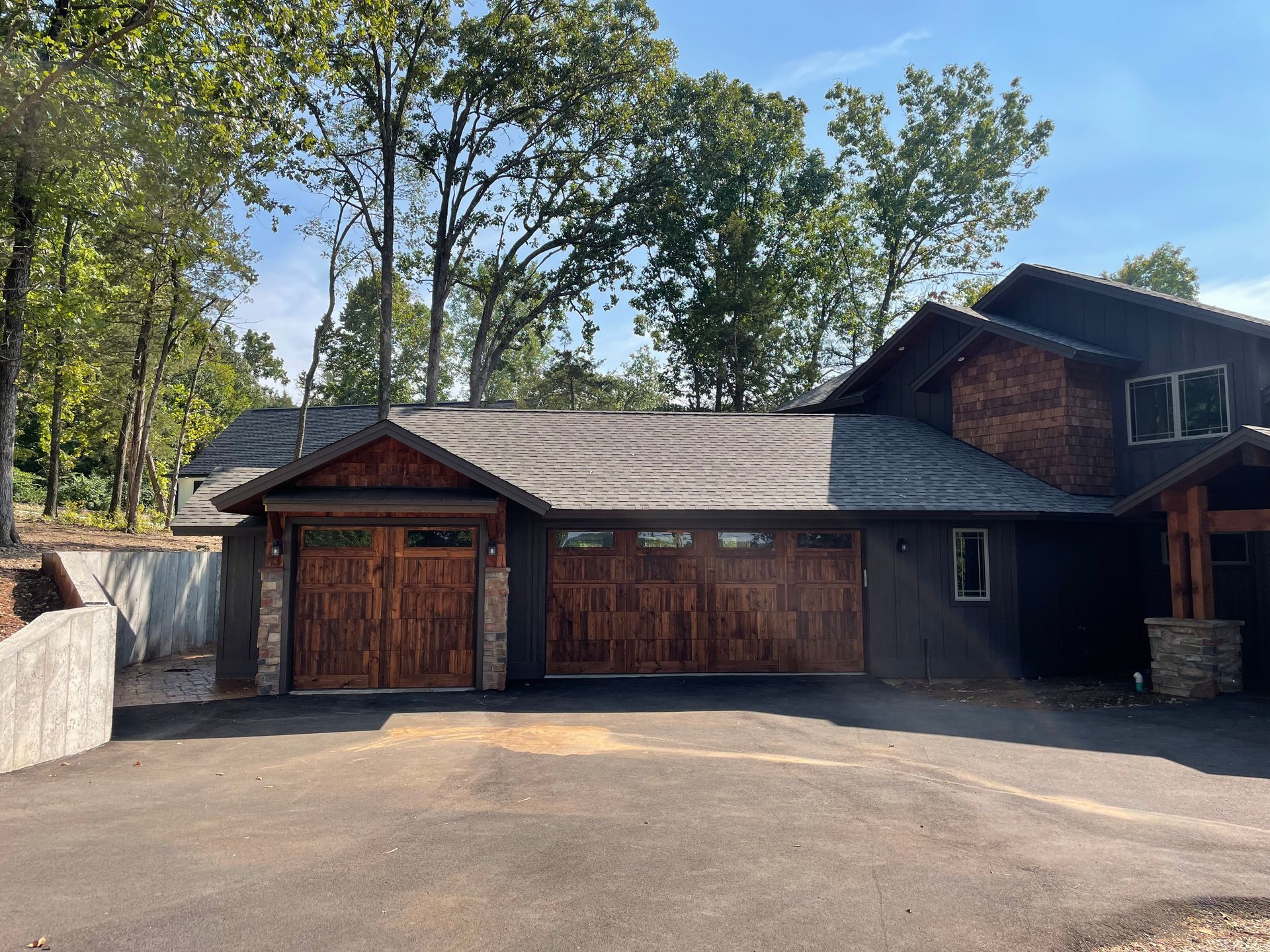 A large house with a wooden garage door is surrounded by trees.