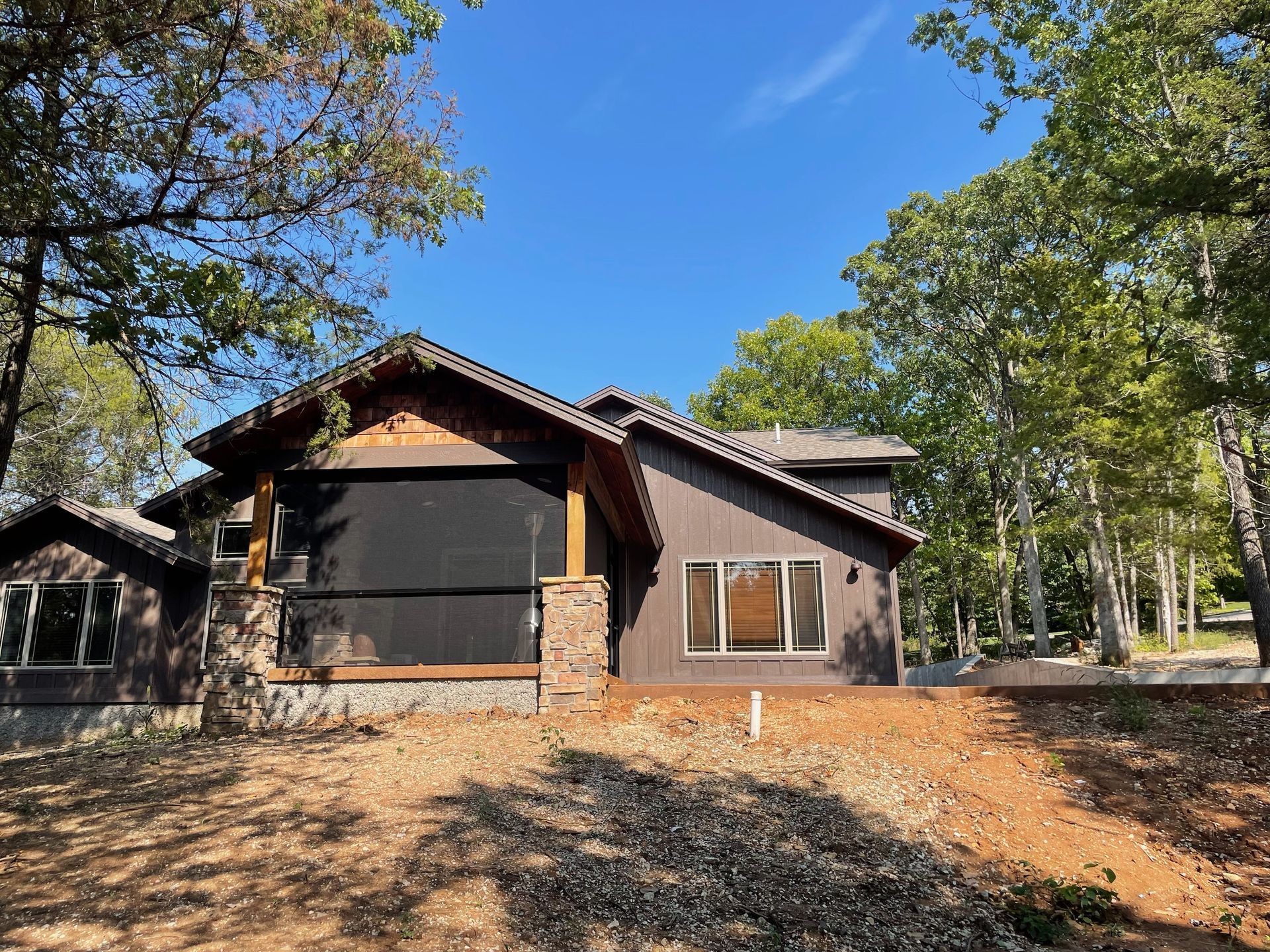 A house with a screened in porch is surrounded by trees on a sunny day.