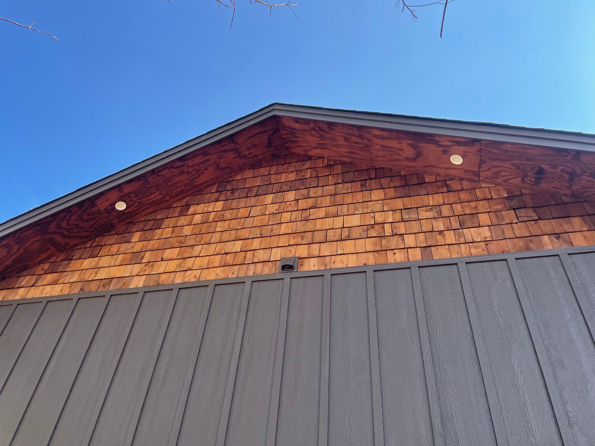 The roof of a building with wooden siding and a blue sky in the background.