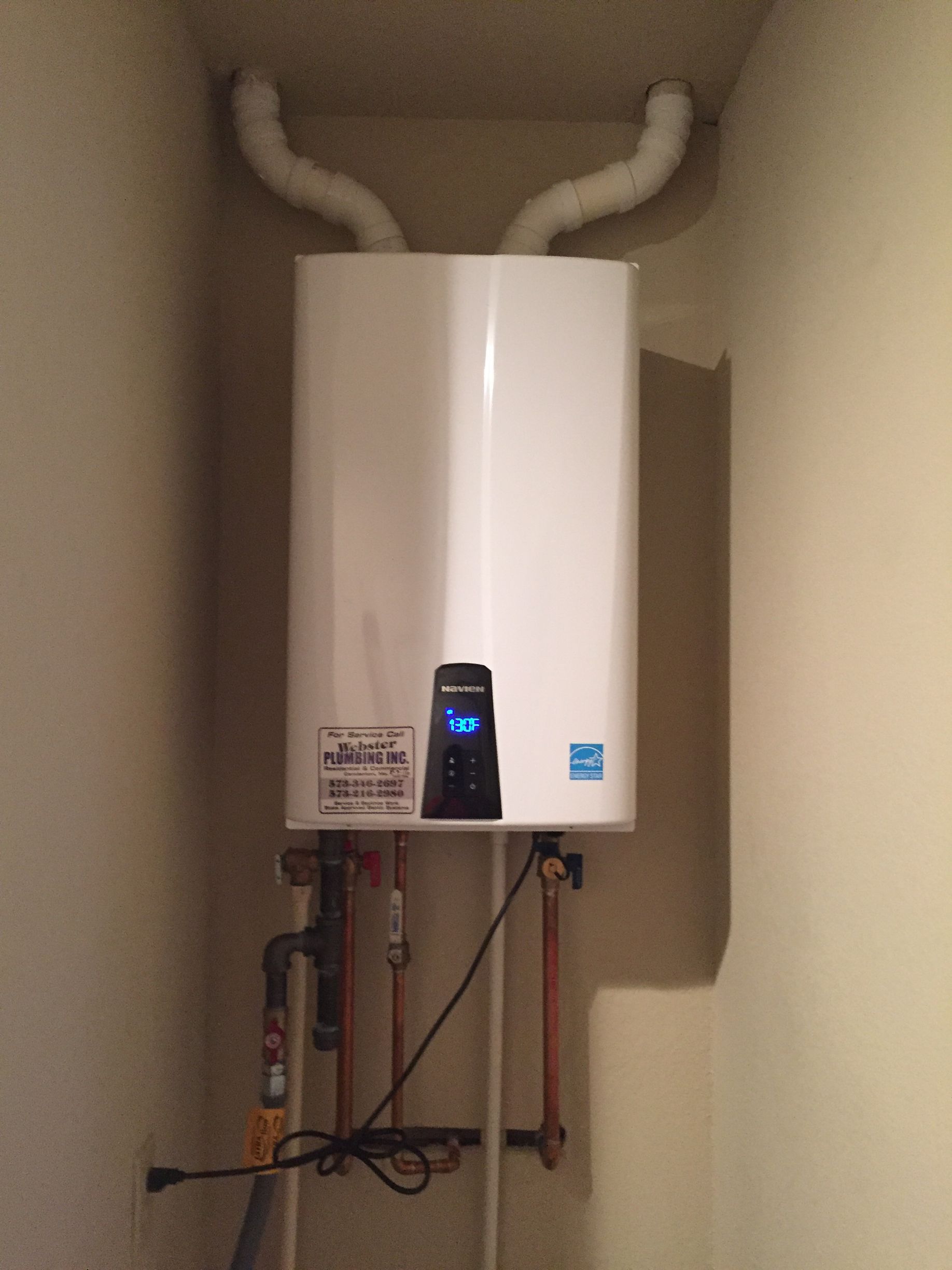 A white water heater is hanging on a wall in a room.
