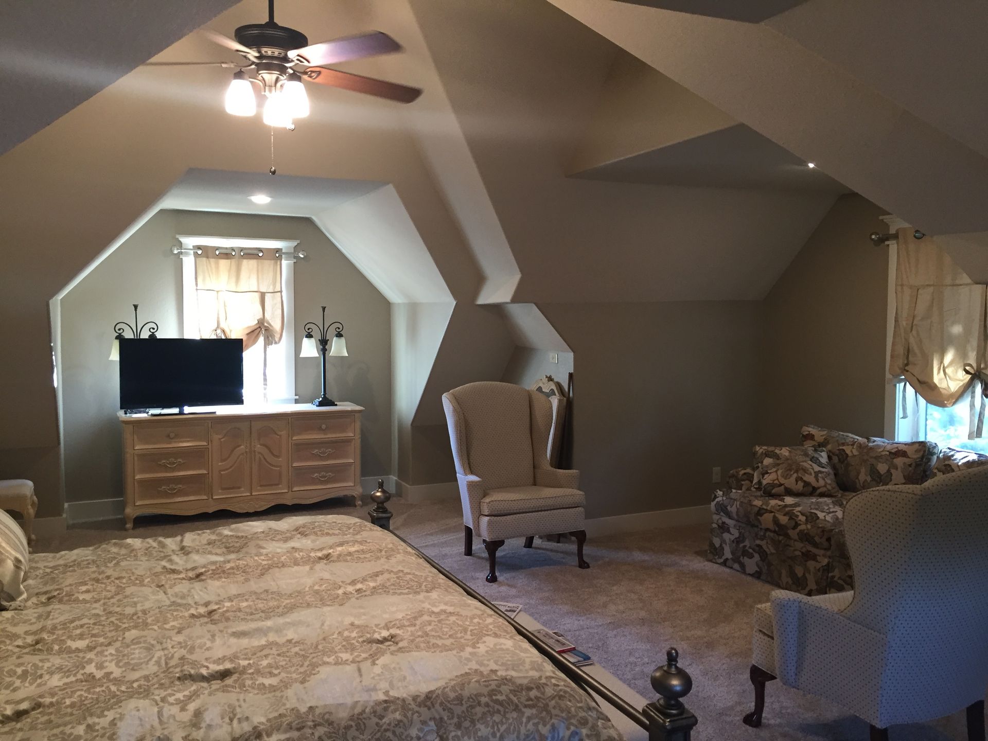 A bedroom with a bed , chairs , a television and a ceiling fan.