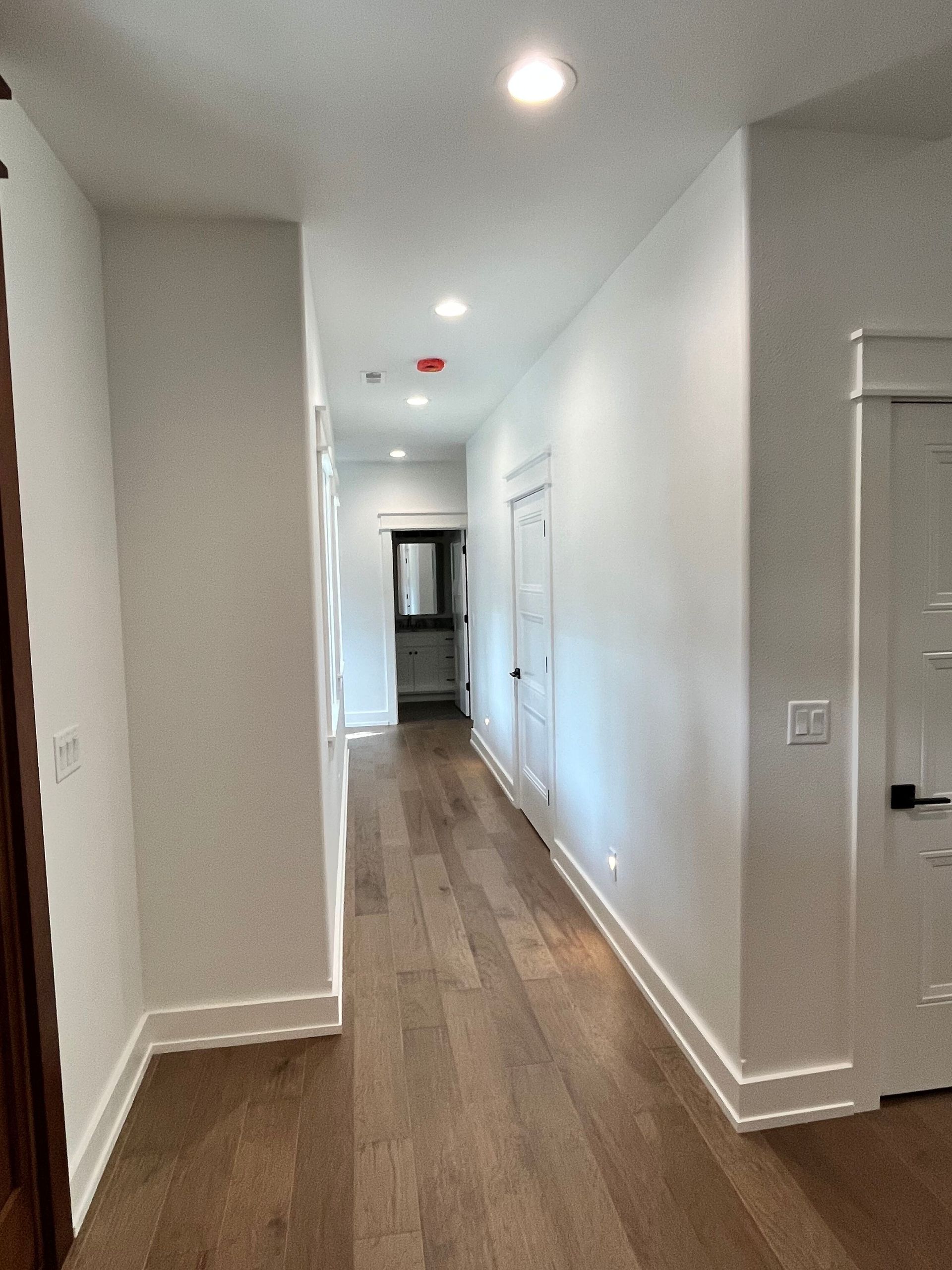 A long hallway with hardwood floors and white walls in a house.