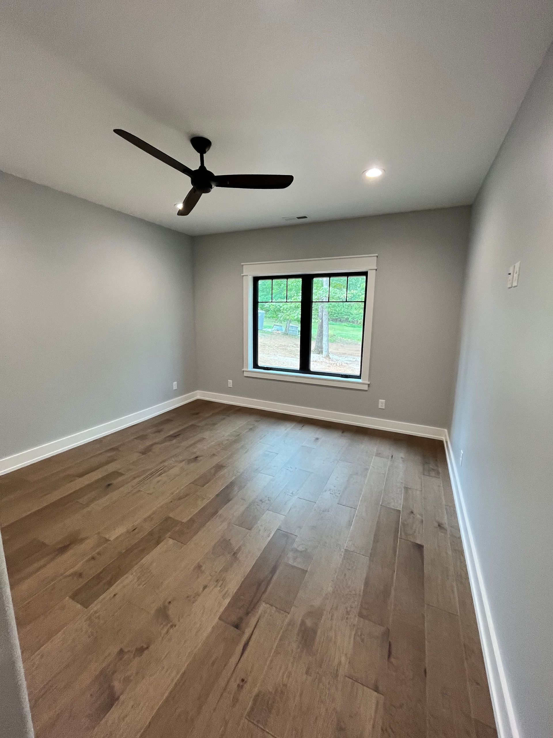 An empty room with hardwood floors and a ceiling fan.