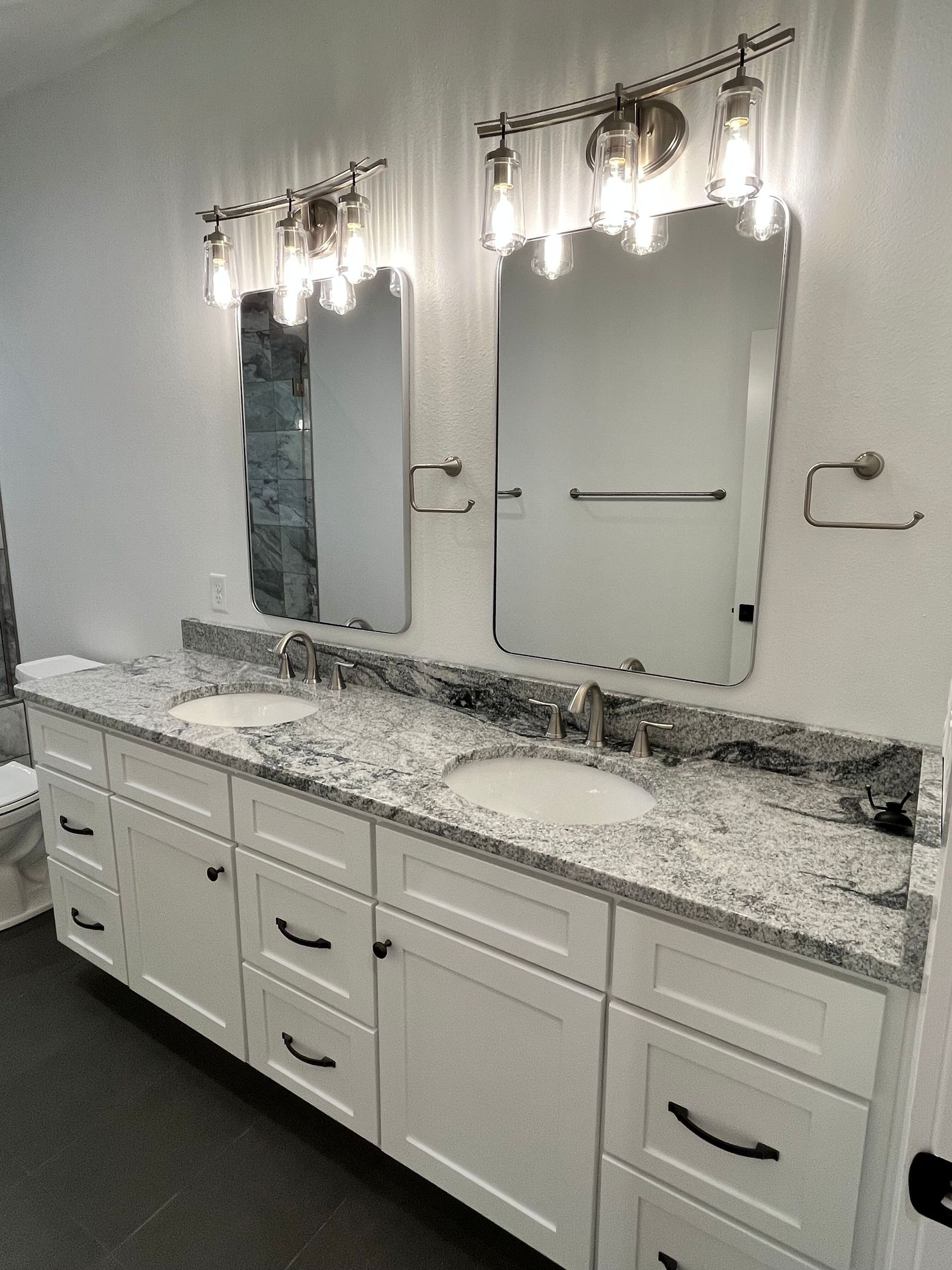 A bathroom with two sinks , two mirrors , and a toilet.