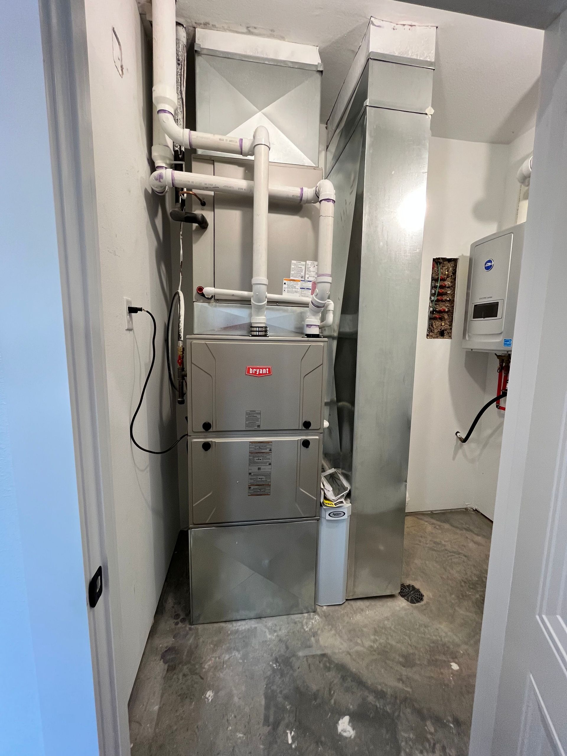 A stainless steel furnace is sitting in a room next to a door.