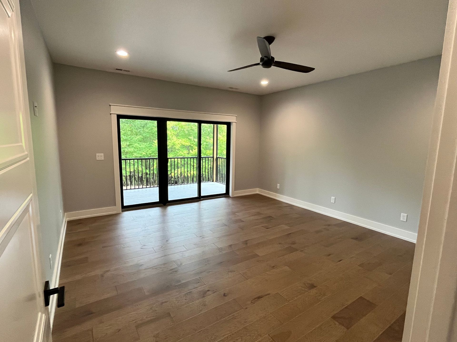 A large empty room with hardwood floors and a ceiling fan.